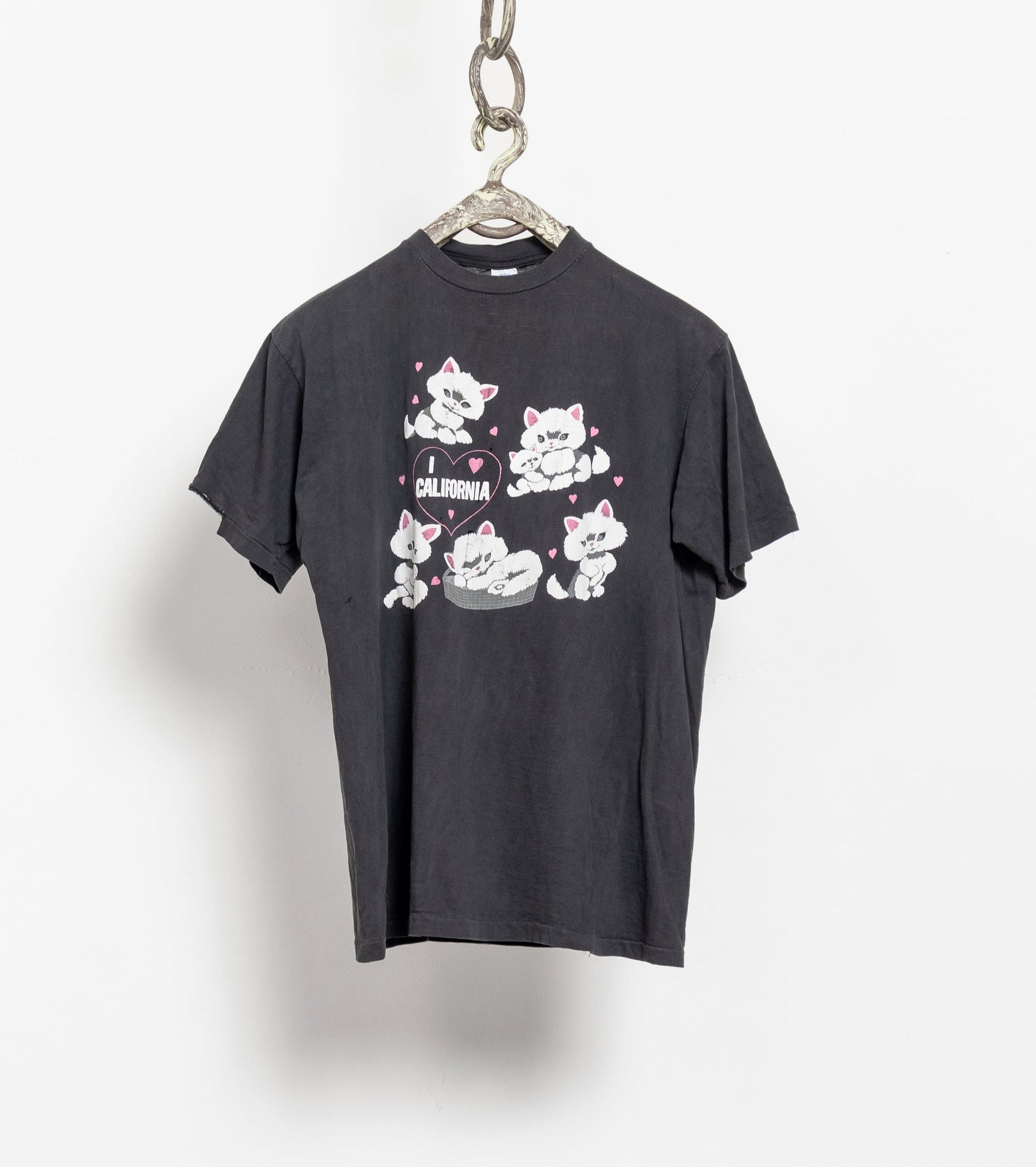 A black t-shirt with a graphic print of cats in the shape of a cat face on the front, displayed on a hanger against a white wall.