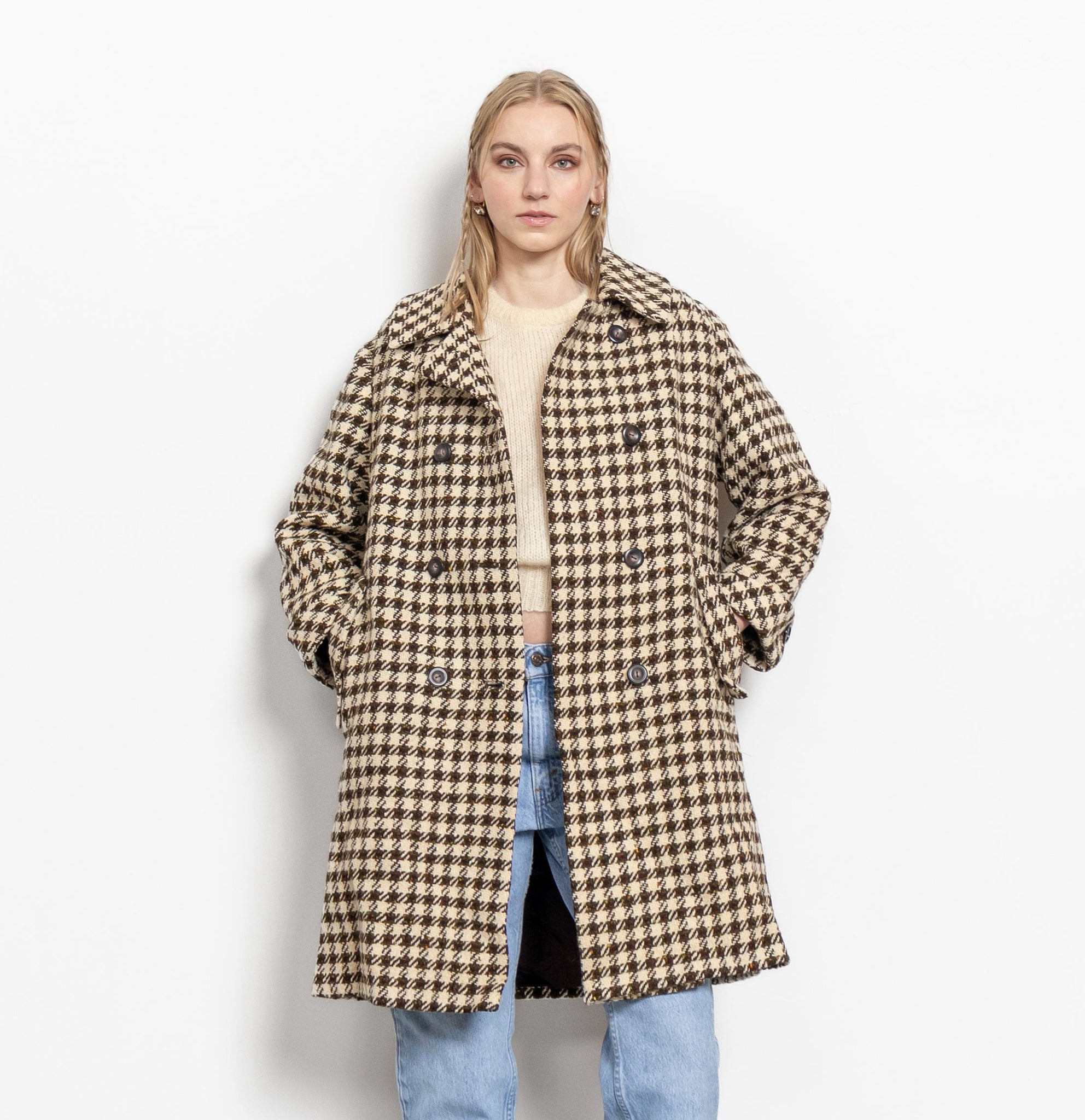 A woman modeling a vintage 1960's style double-breasted, checkered coat in beige and brown colors, with side pockets and cuffed sleeves.