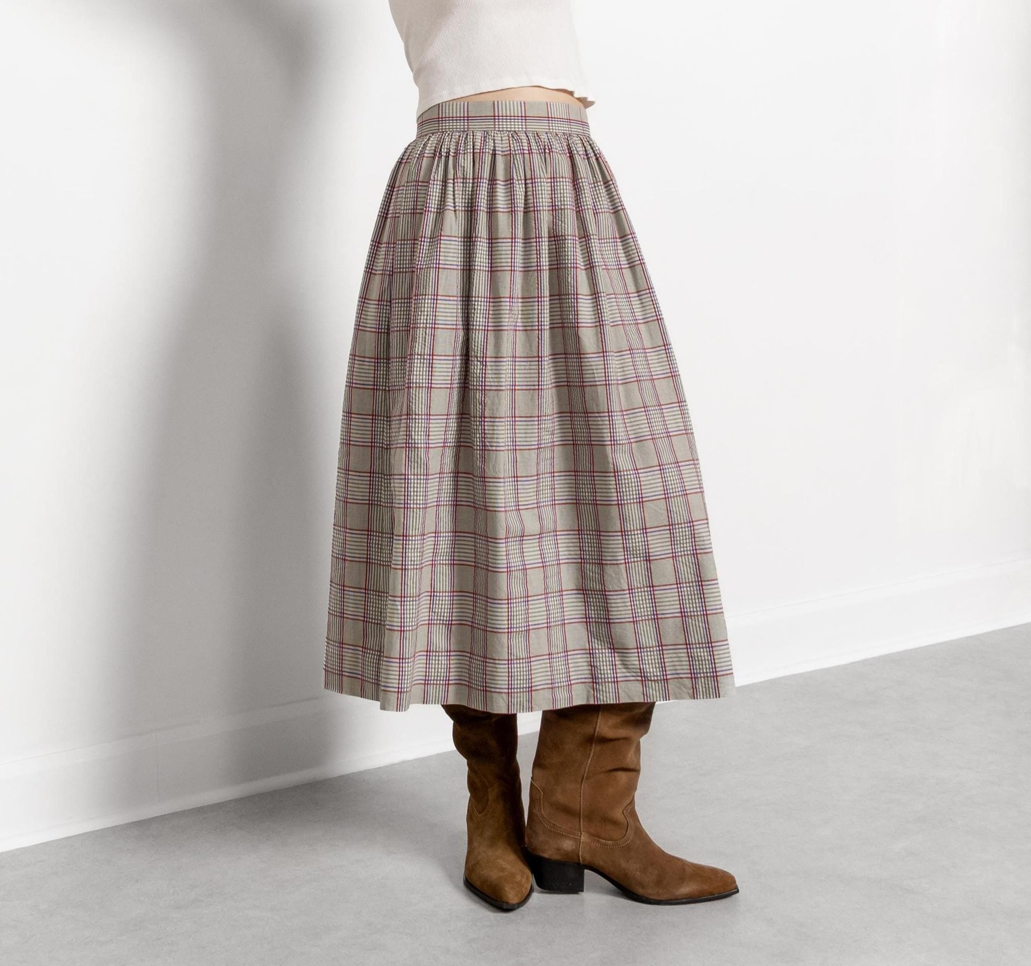 A person wearing a vintage high-waisted plaid maxi skirt in brown and beige, with buttons up at the waist, paired with brown boots.
