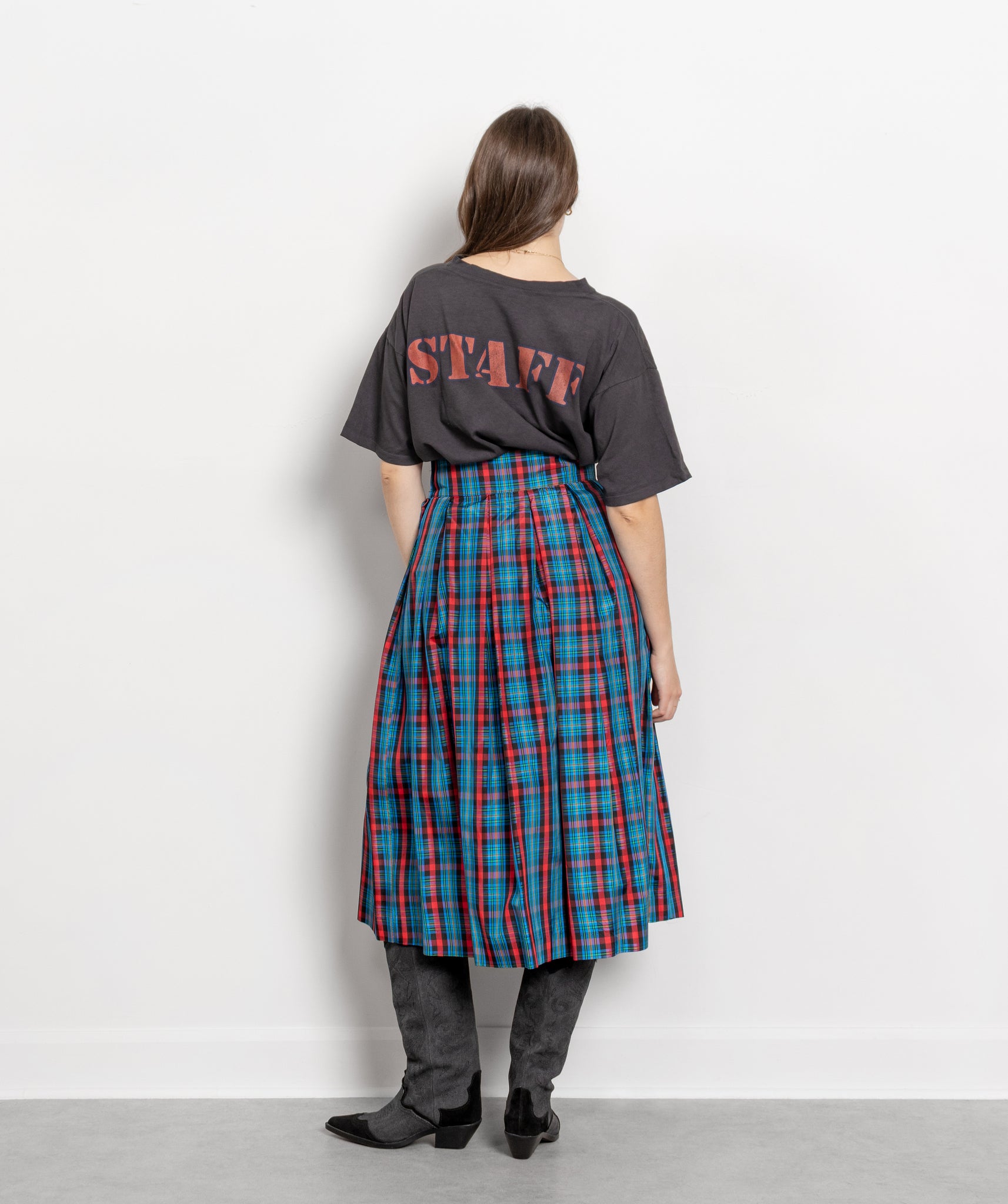 Person wearing a dark gray t-shirt with 'STAFF' printed on the back and a plaid skirt.