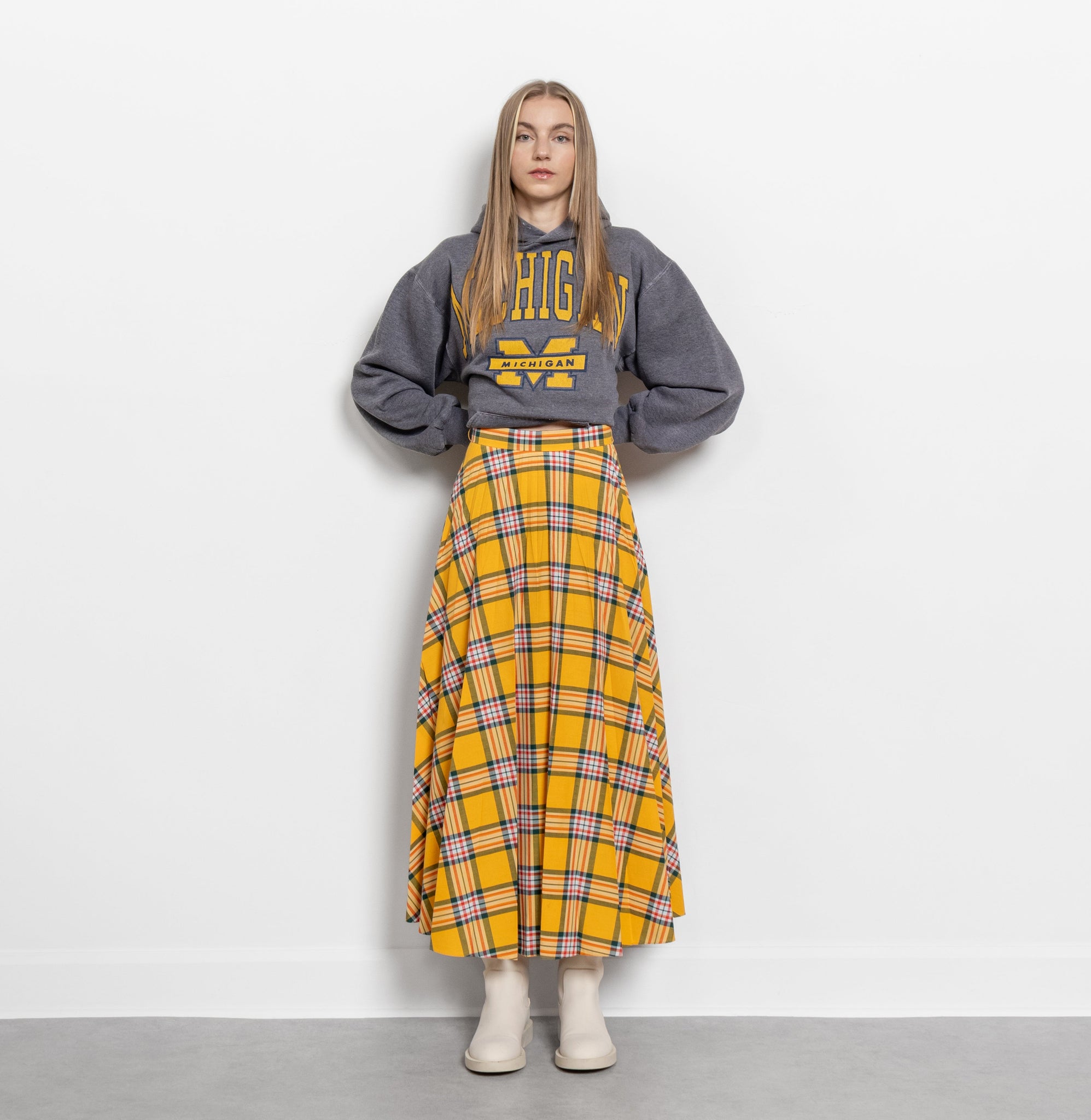 Person wearing a gray sweatshirt with text and a yellow plaid skirt on a white background