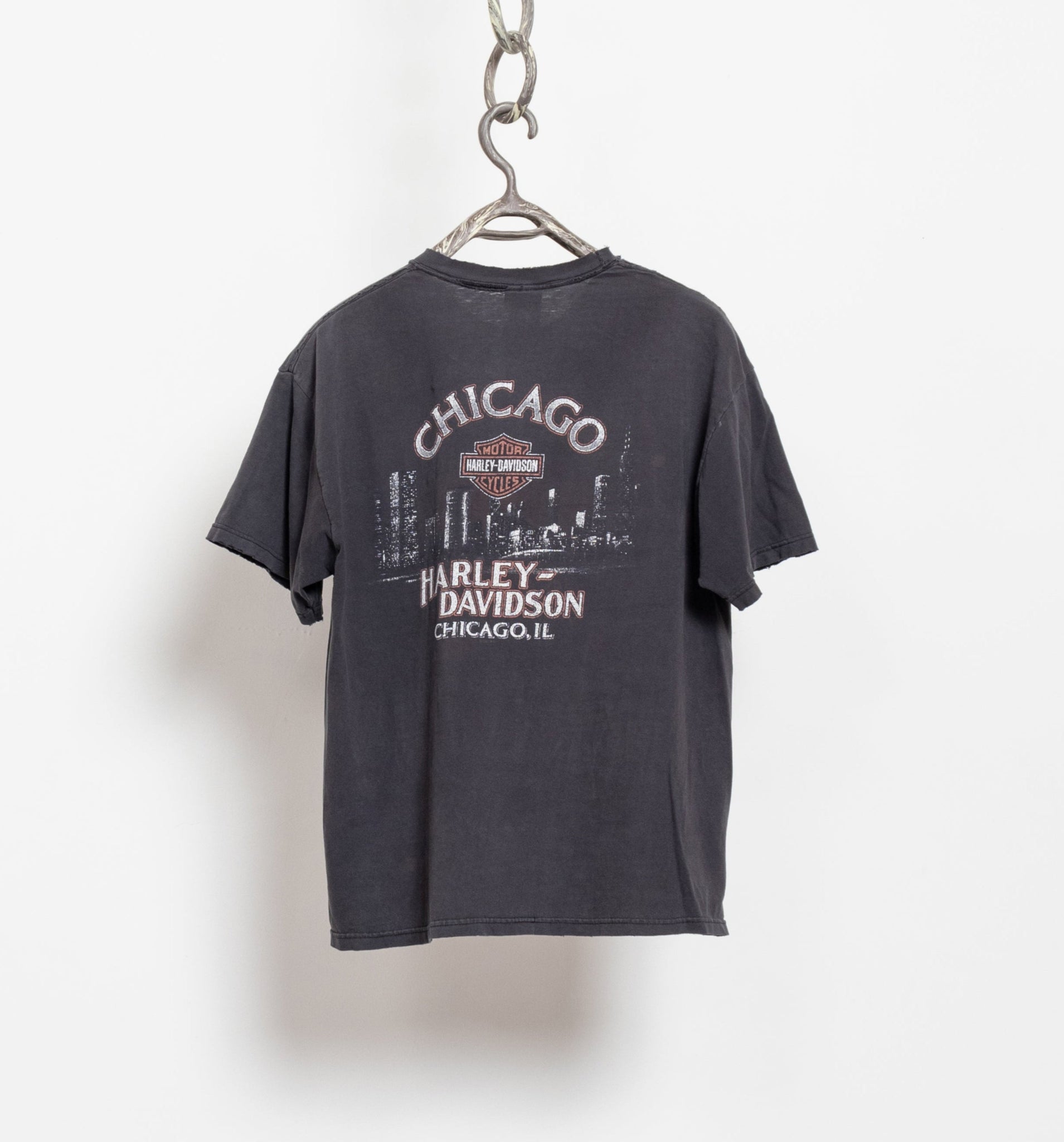 A vintage 90's Harley Davidson t-shirt with the Chicago skyline printed on the back, hanging on a hanger against a white background.
