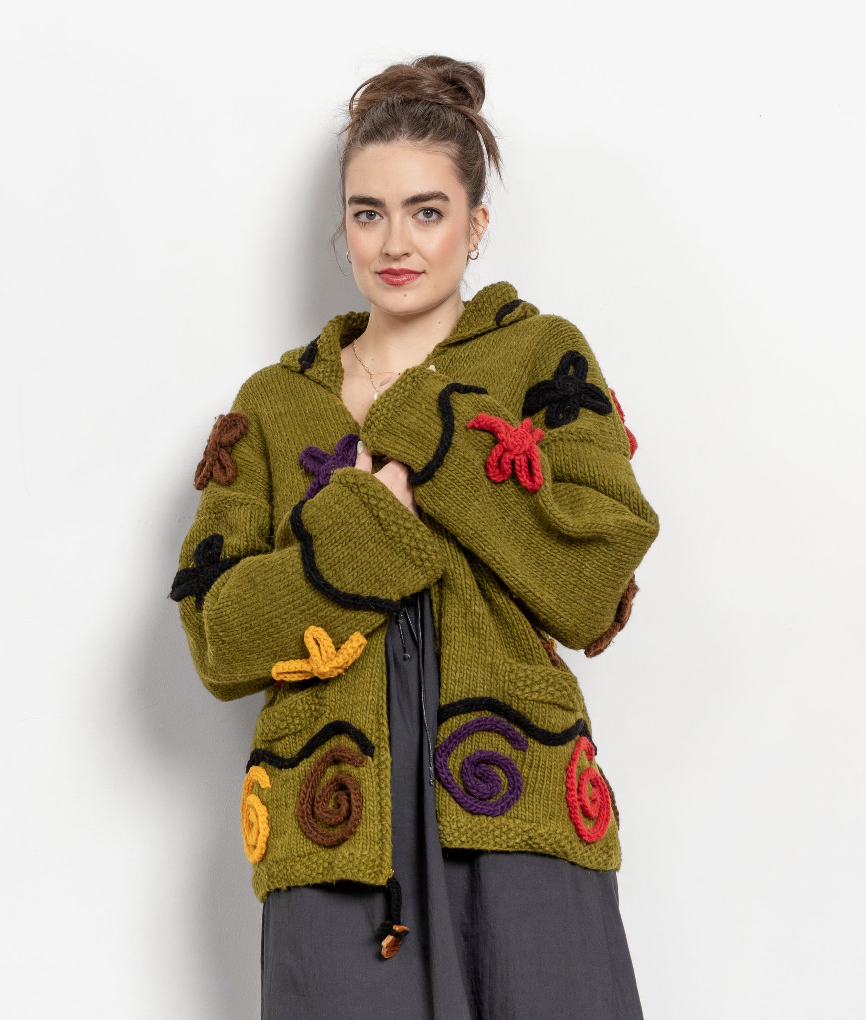 Woman wearing a green knitted jacket with colorful patterns on a white background