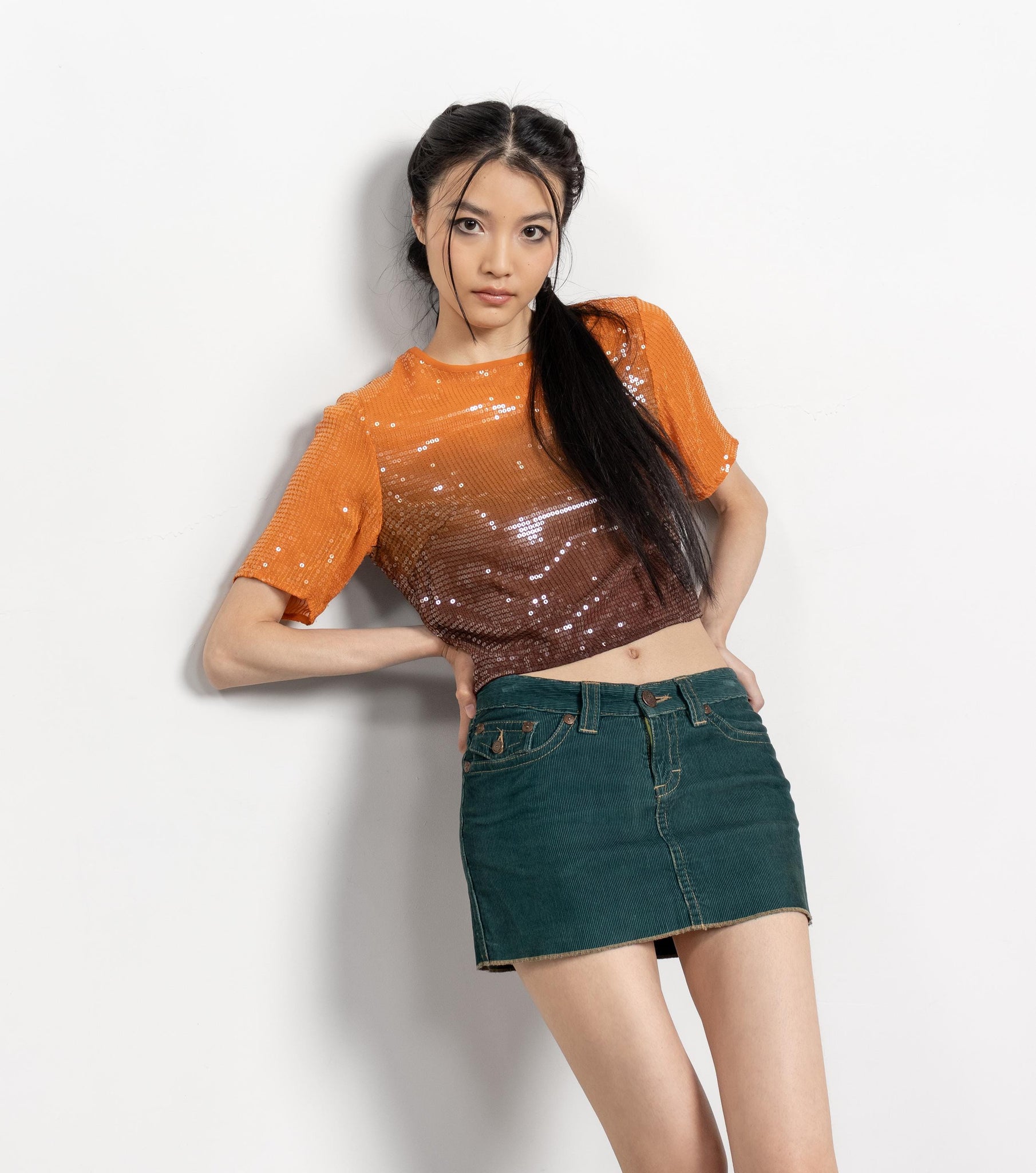 Woman wearing an orange and brown gradient top with a green skirt on a white background
