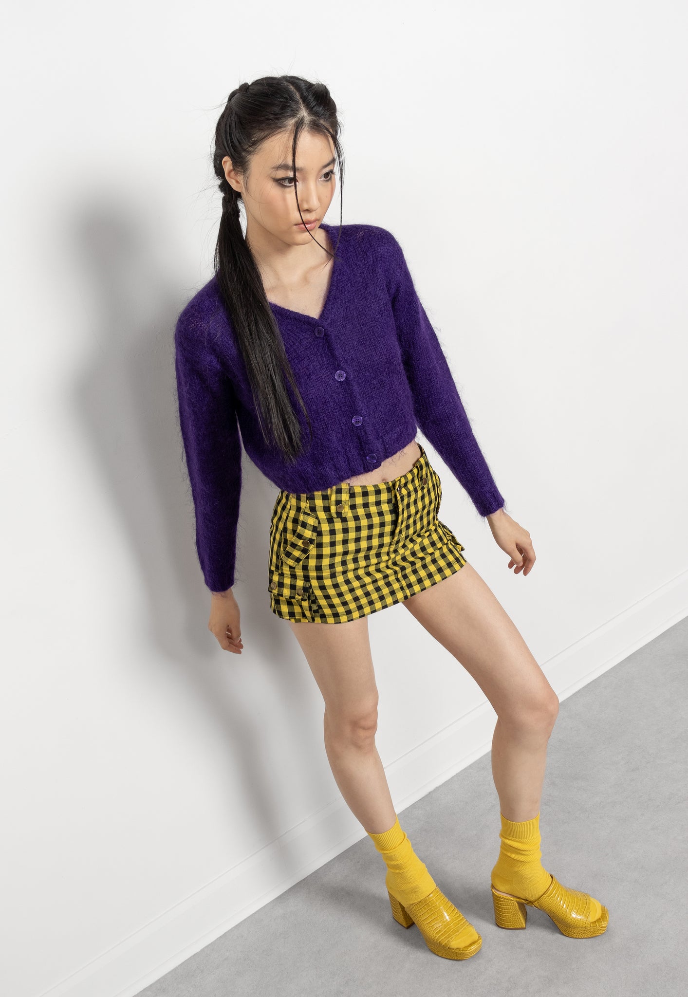 Woman wearing a purple cardigan, yellow checkered skirt, and yellow boots on a white background
