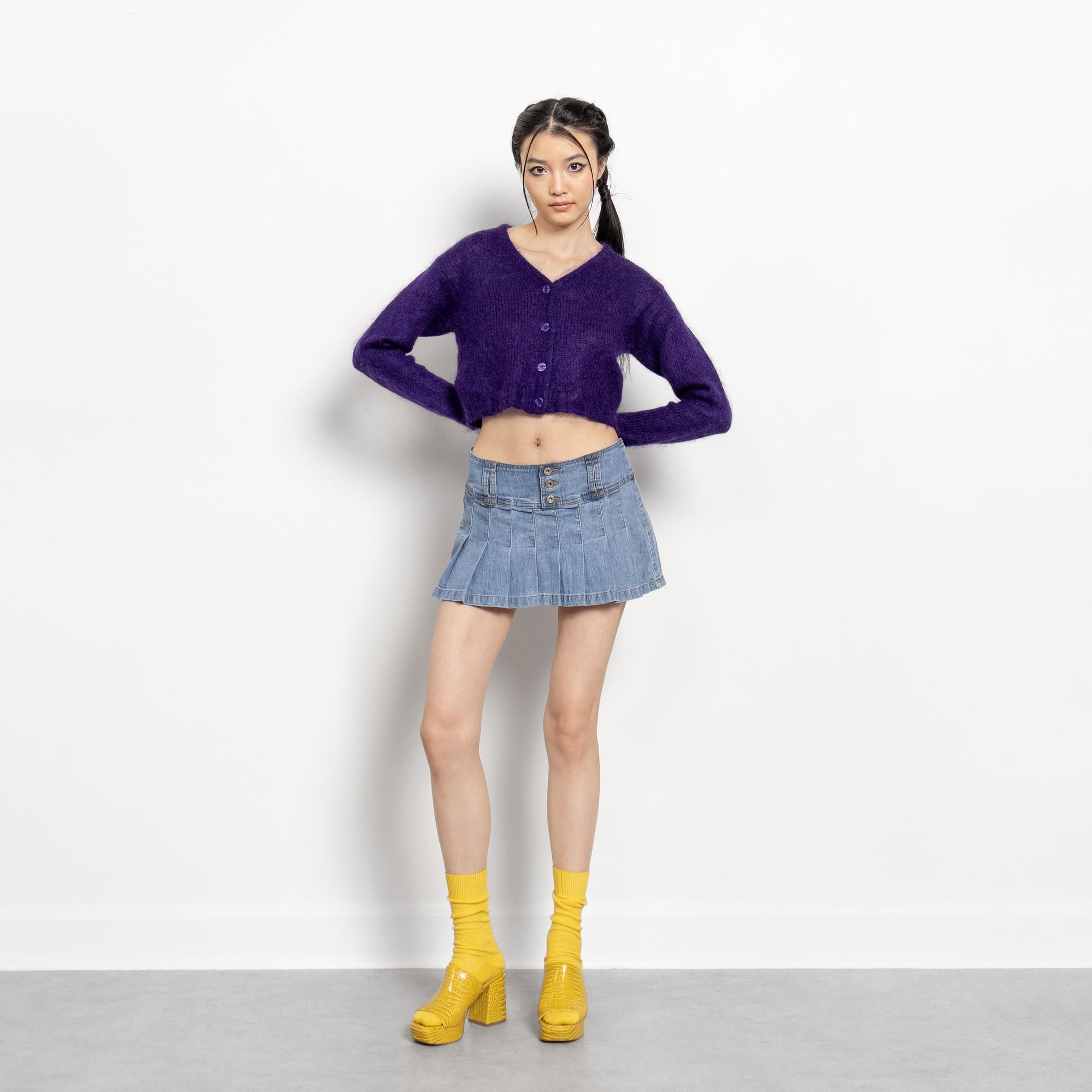Woman wearing a purple cardigan, blue denim skirt, and yellow boots on a white background