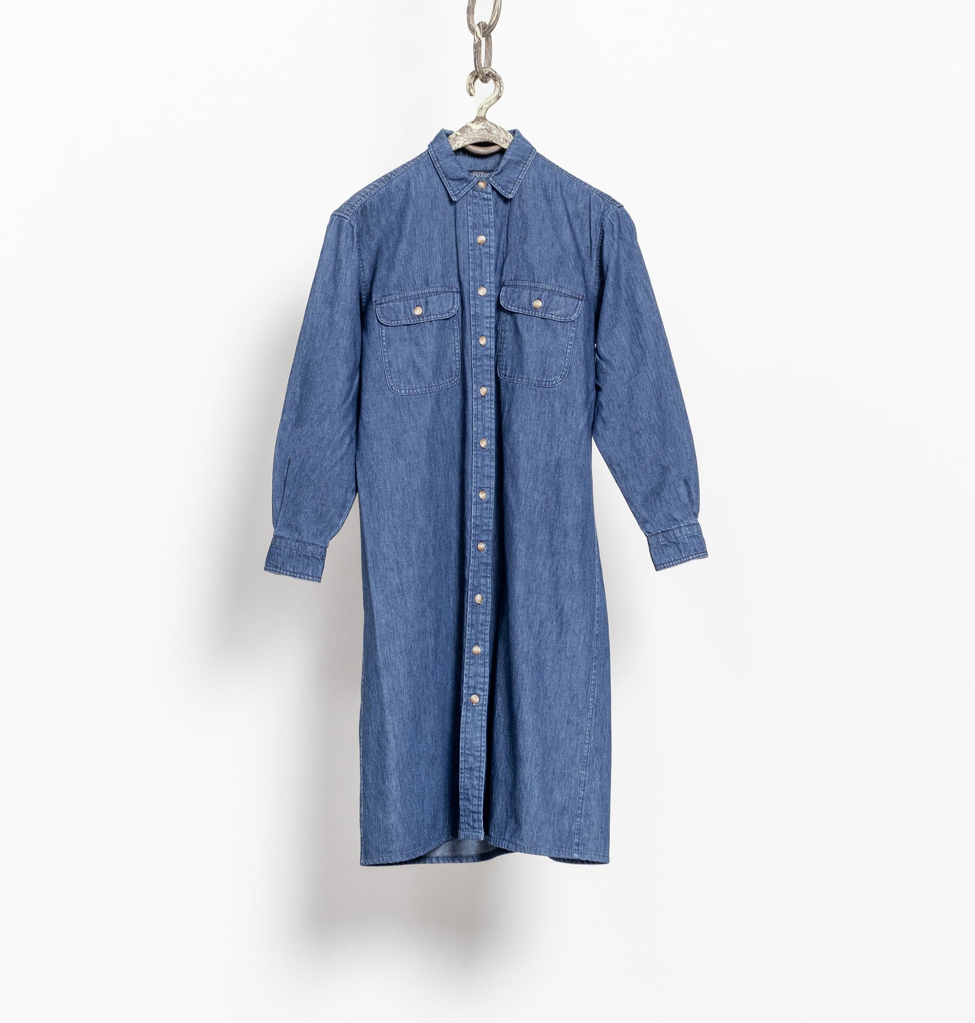A vintage long sleeve denim midi dress with a classic collar, front pockets, and side pockets, displayed on a hanger against a white background.
