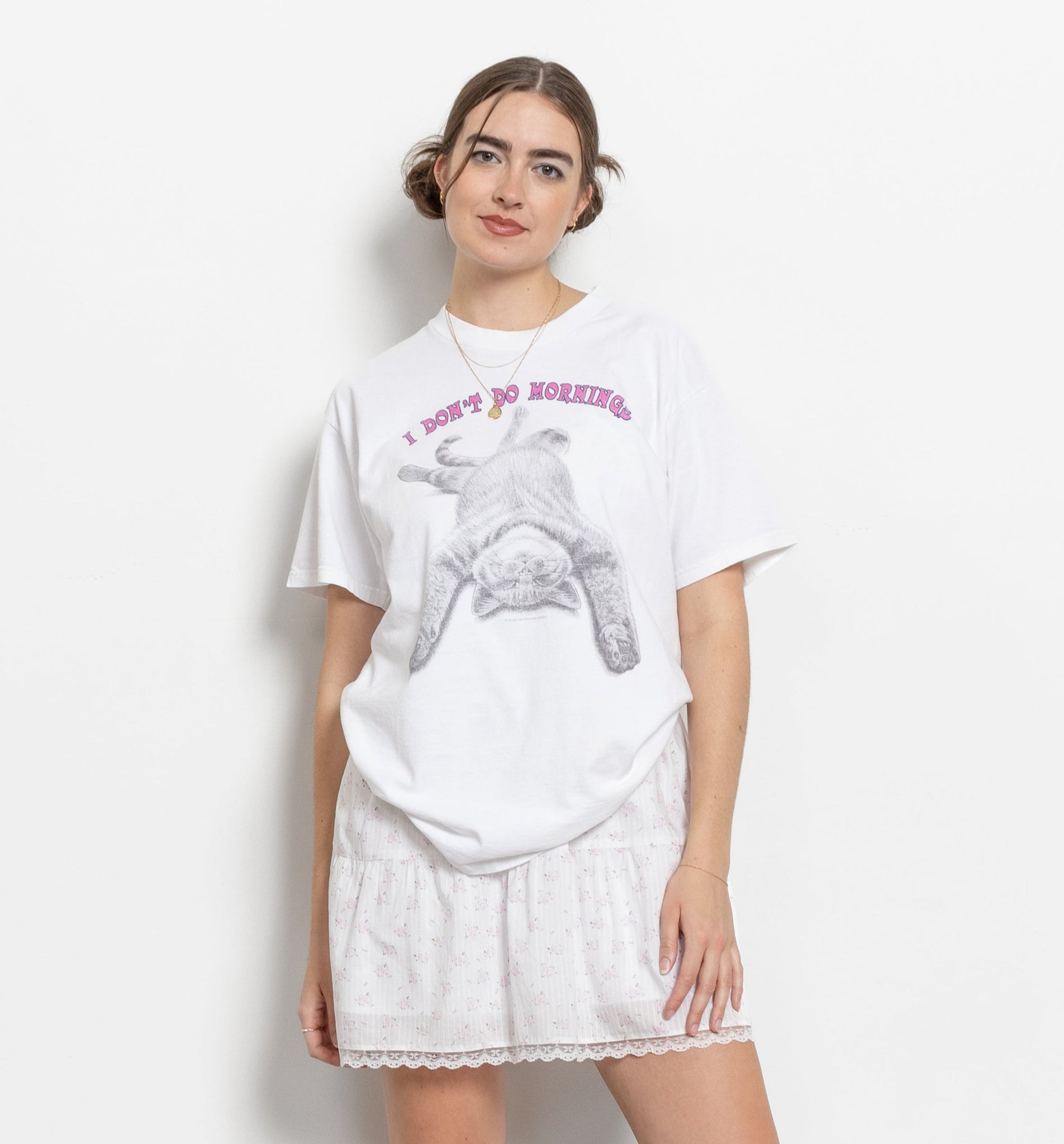 A person wearing a white crew neck t-shirt with a graphic that says 'Don't Do Mornings' and an image of a kitty cat.