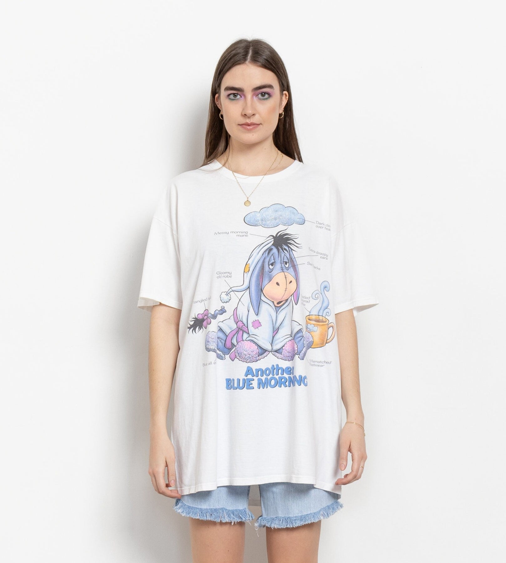 A person wearing a white oversized t-shirt with a graphic of Eeyore from Winnie the Pooh. The t-shirt has the text 'Another Blue Monday' on it.