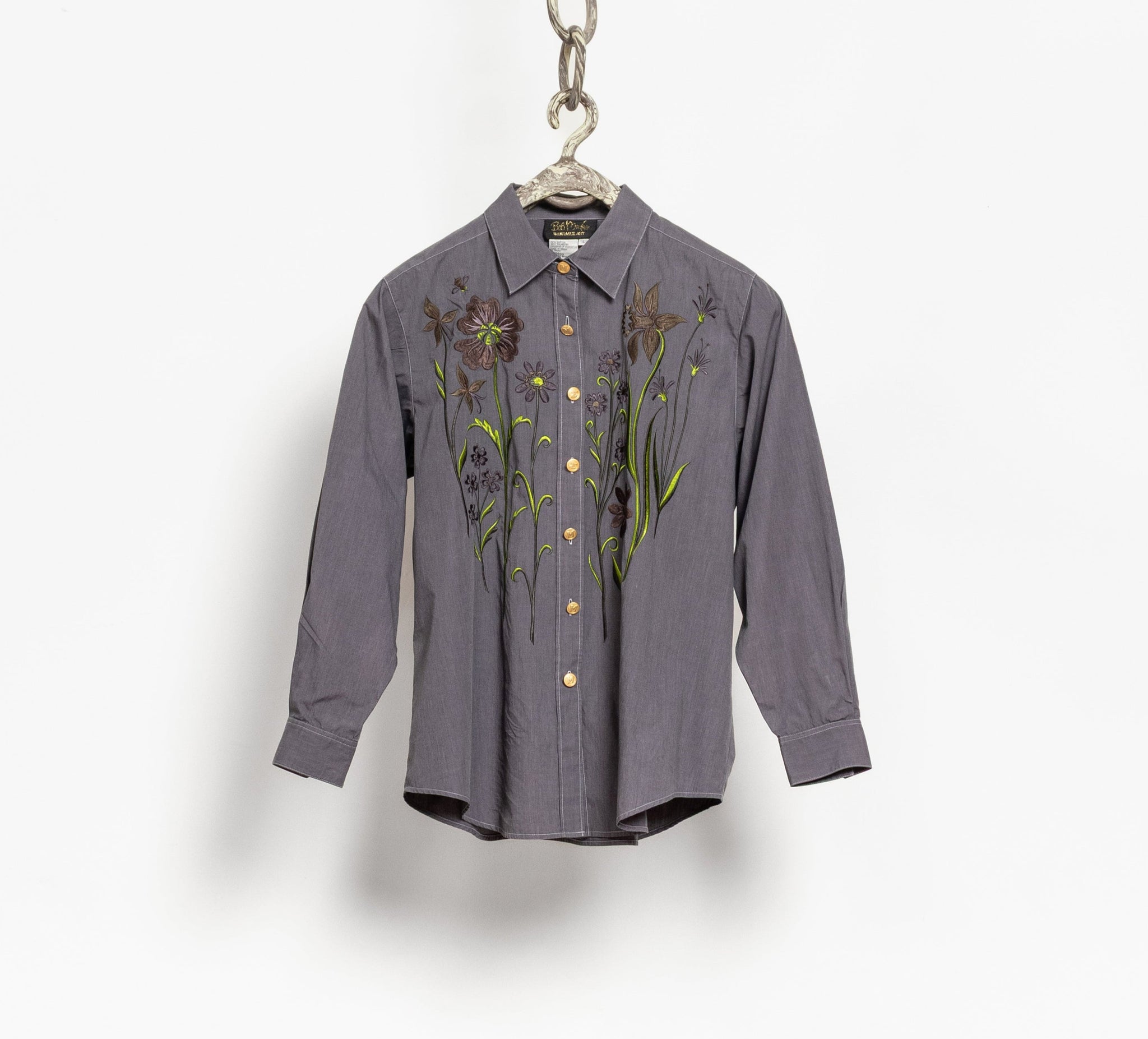 Gray shirt with floral embroidery on a hanger against a white background