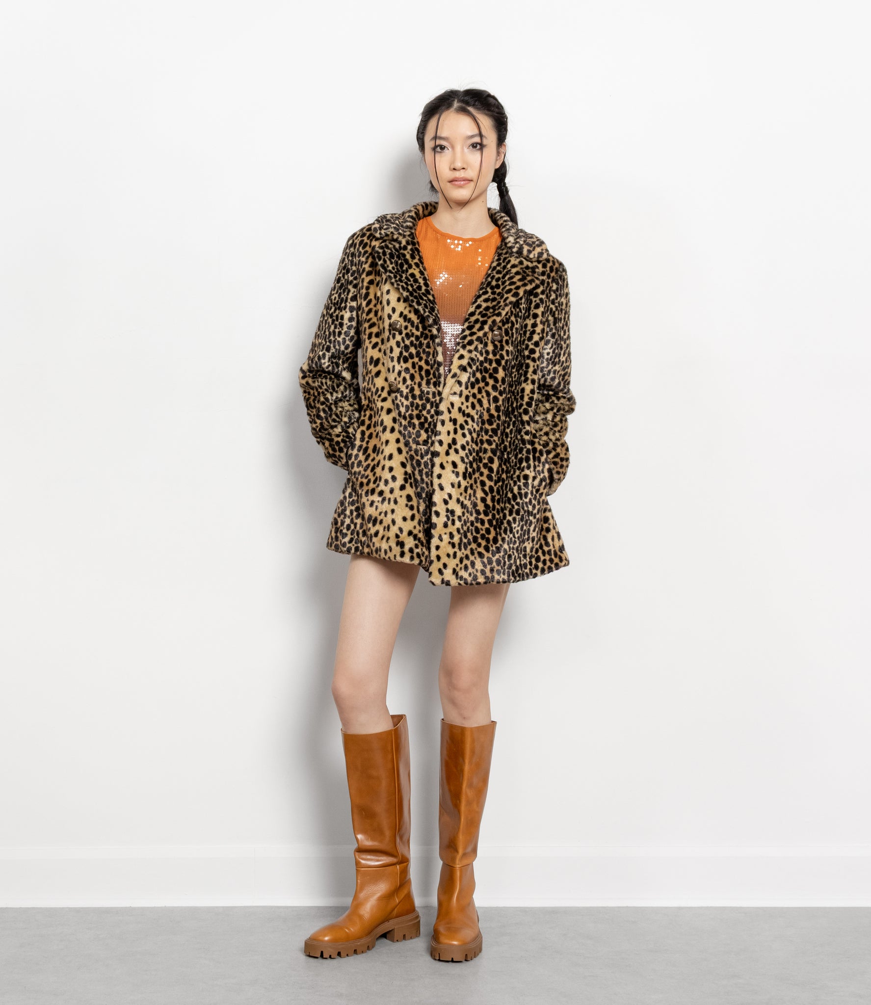 Person wearing a leopard print coat and brown knee-high boots on a white background