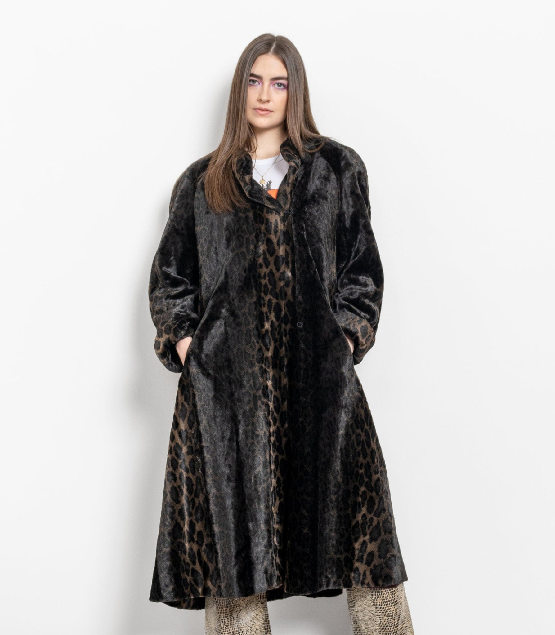 Person wearing a long dark coat with leopard print pattern on a white background