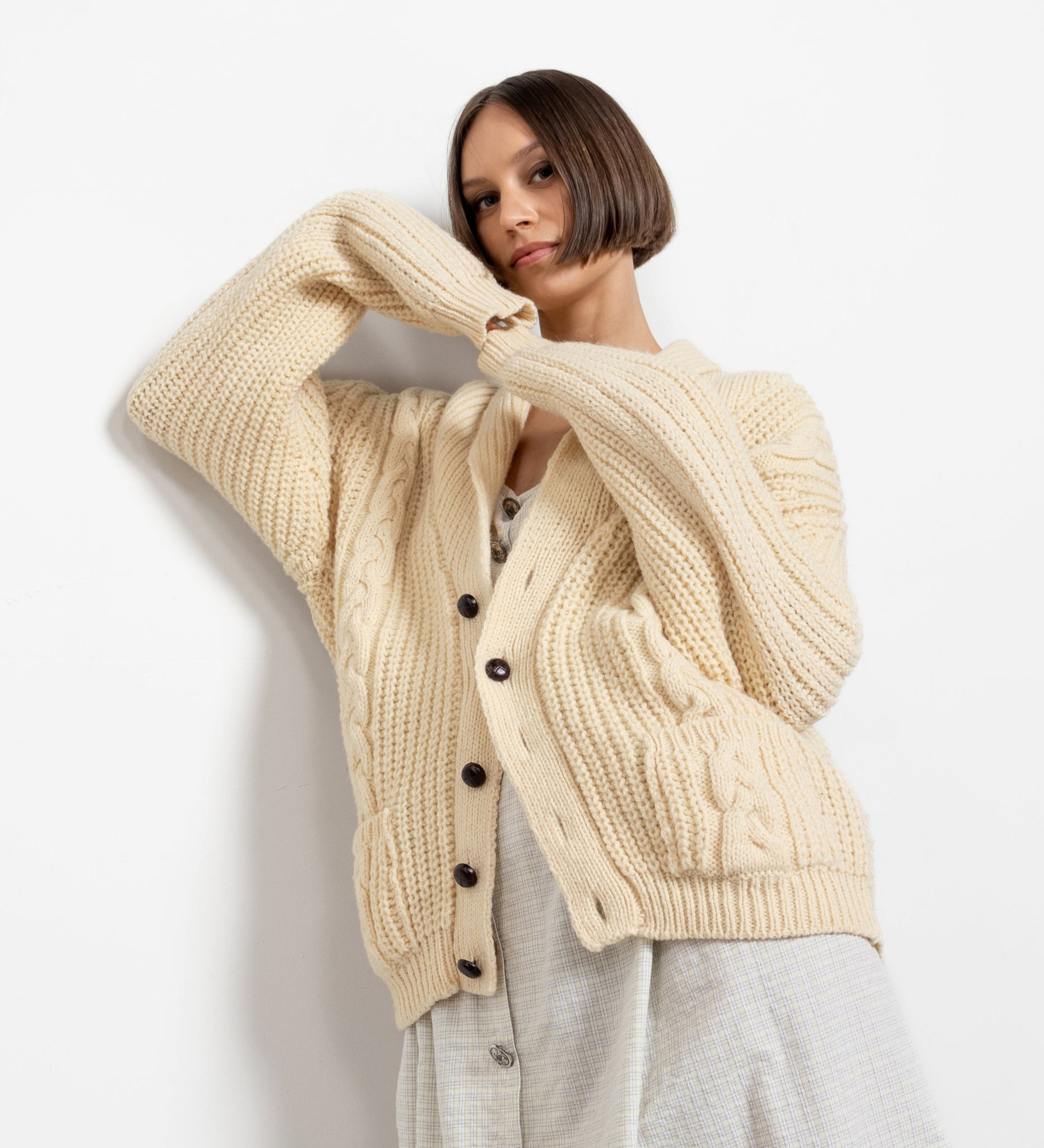 A woman wearing a vintage 100% wool cream cable knit traditional Irish cardigan with wooden buttons, over a white top and a grey skirt.