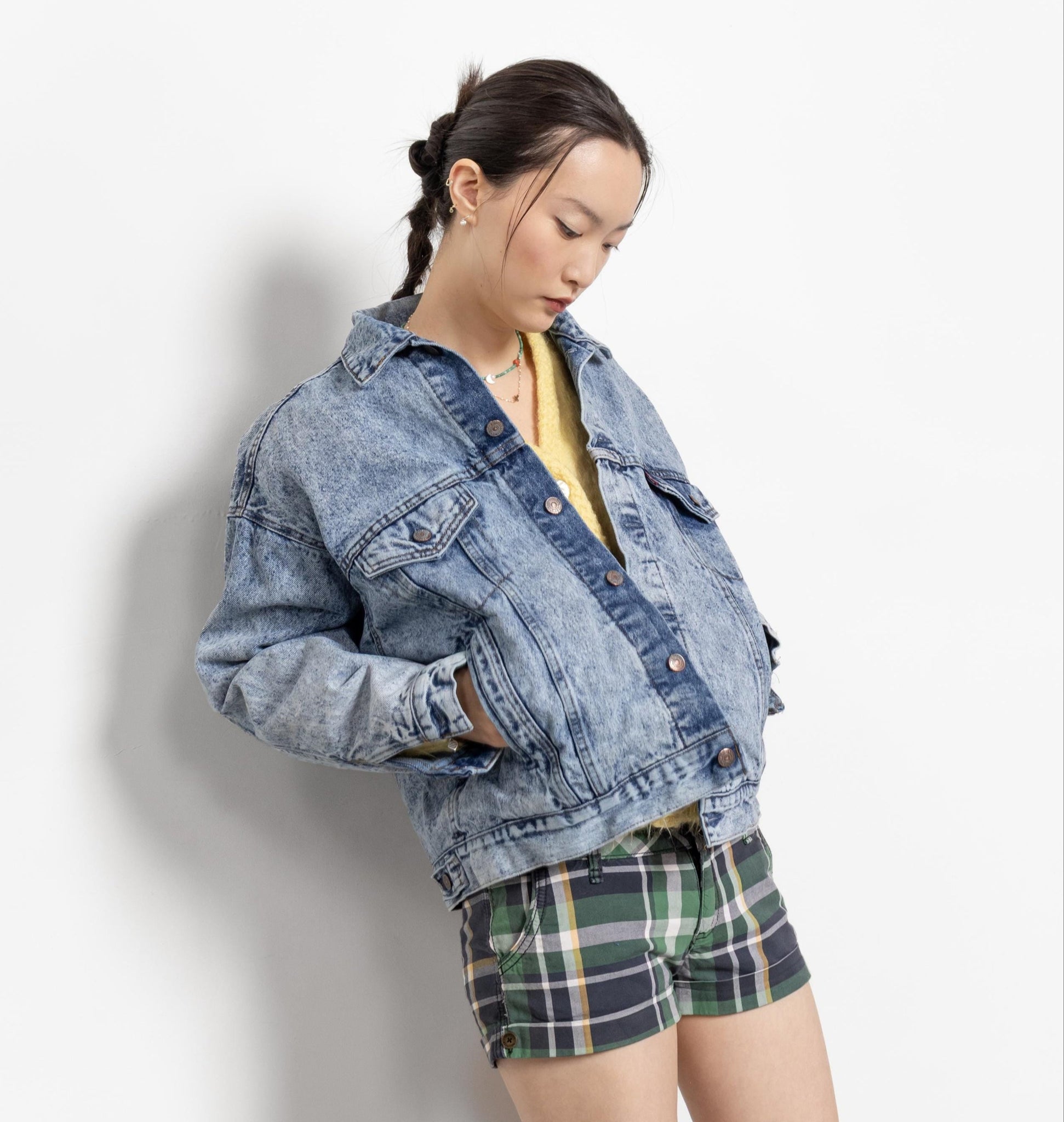 Person wearing a denim jacket and plaid shorts against a white background
