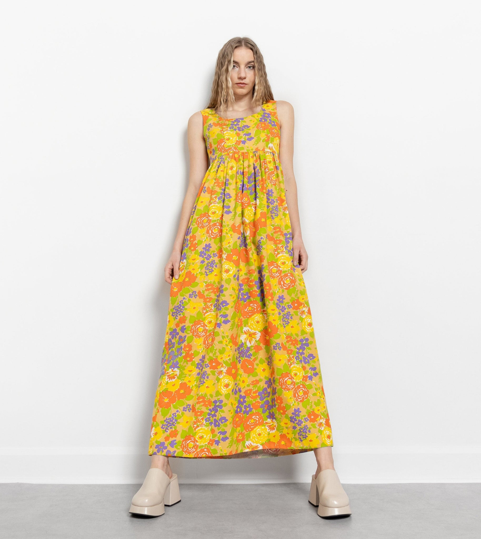 A model wearing a vintage yellow floral sleeveless maxi dress with a floral crinkle pattern, posing against a white background.