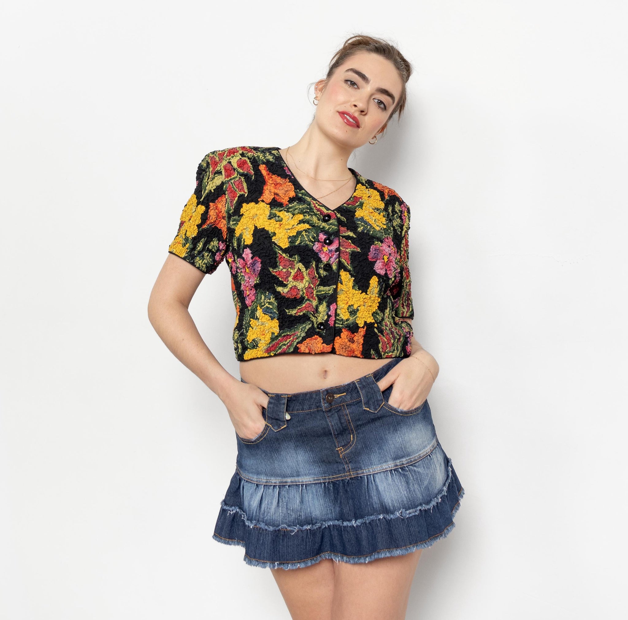 Woman wearing a colorful floral top and denim skirt on a white background