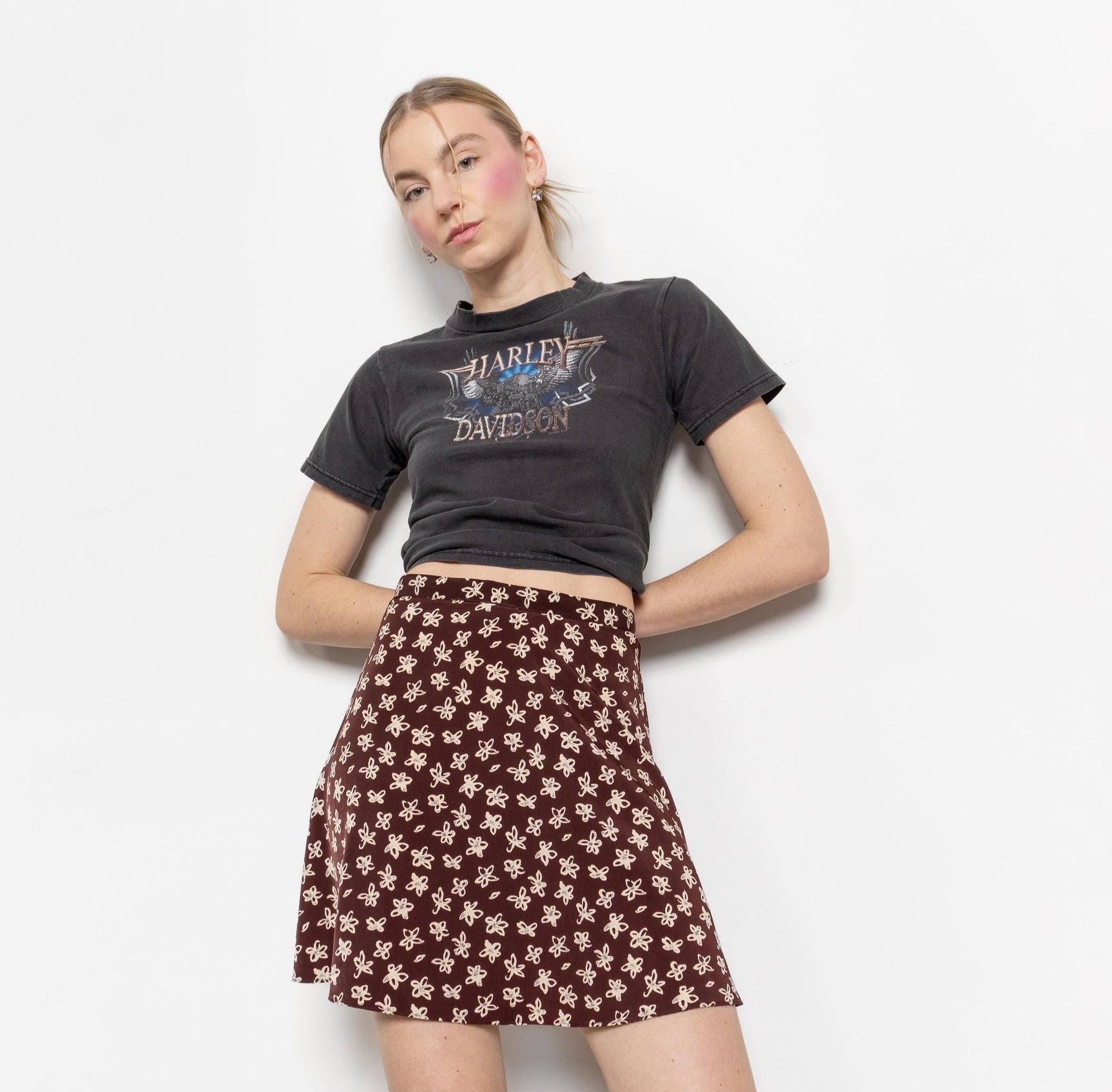 Person wearing a dark gray t-shirt with a graphic design and a brown floral skirt on a white background