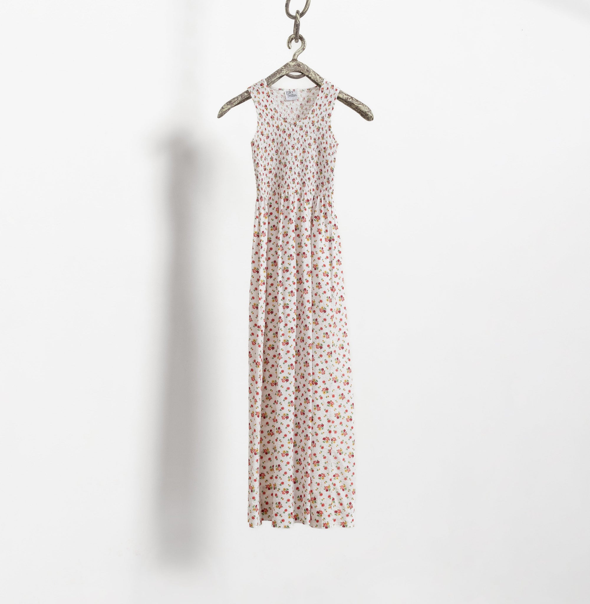 A vintage 80's floral maxi dress in pink and white, hanging on a hanger against a white wall.
