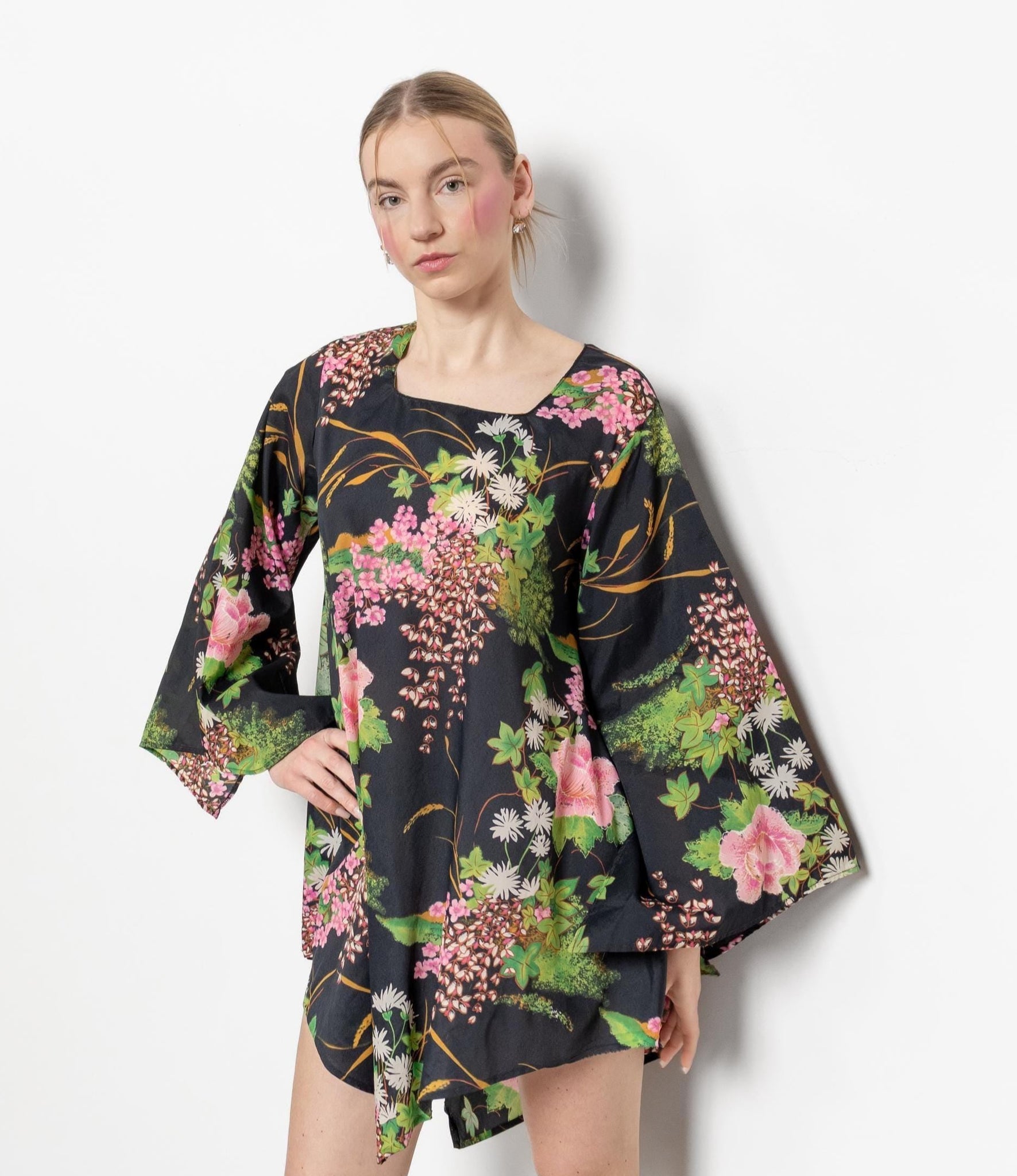 A person wearing a vintage black floral mini tent dress with long bell sleeves and a square neckline. They are paired with white boots and standing against a white background.