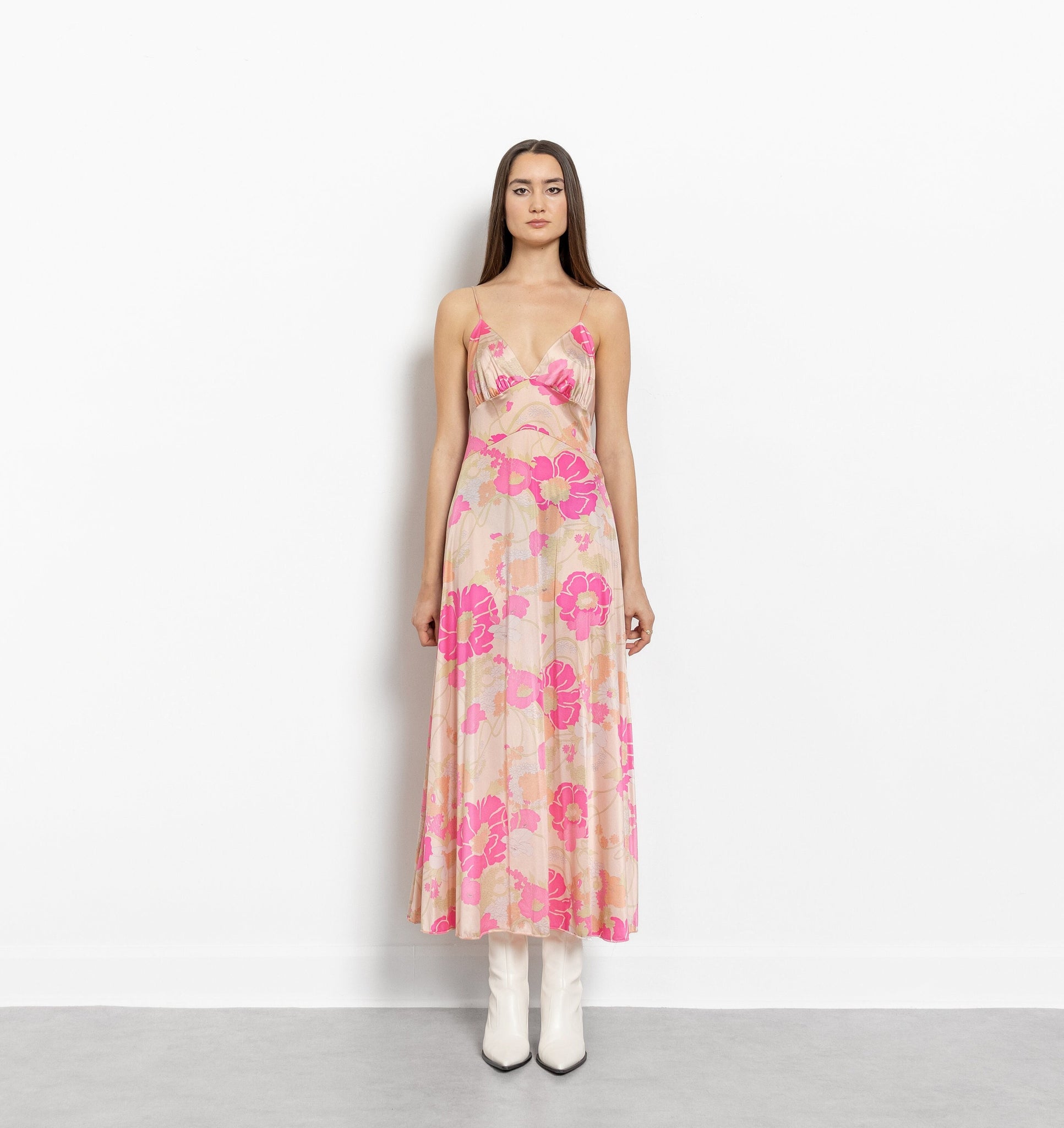 A model wearing a vintage 70's pink floral print maxi dress with spaghetti straps, posing against a white background.