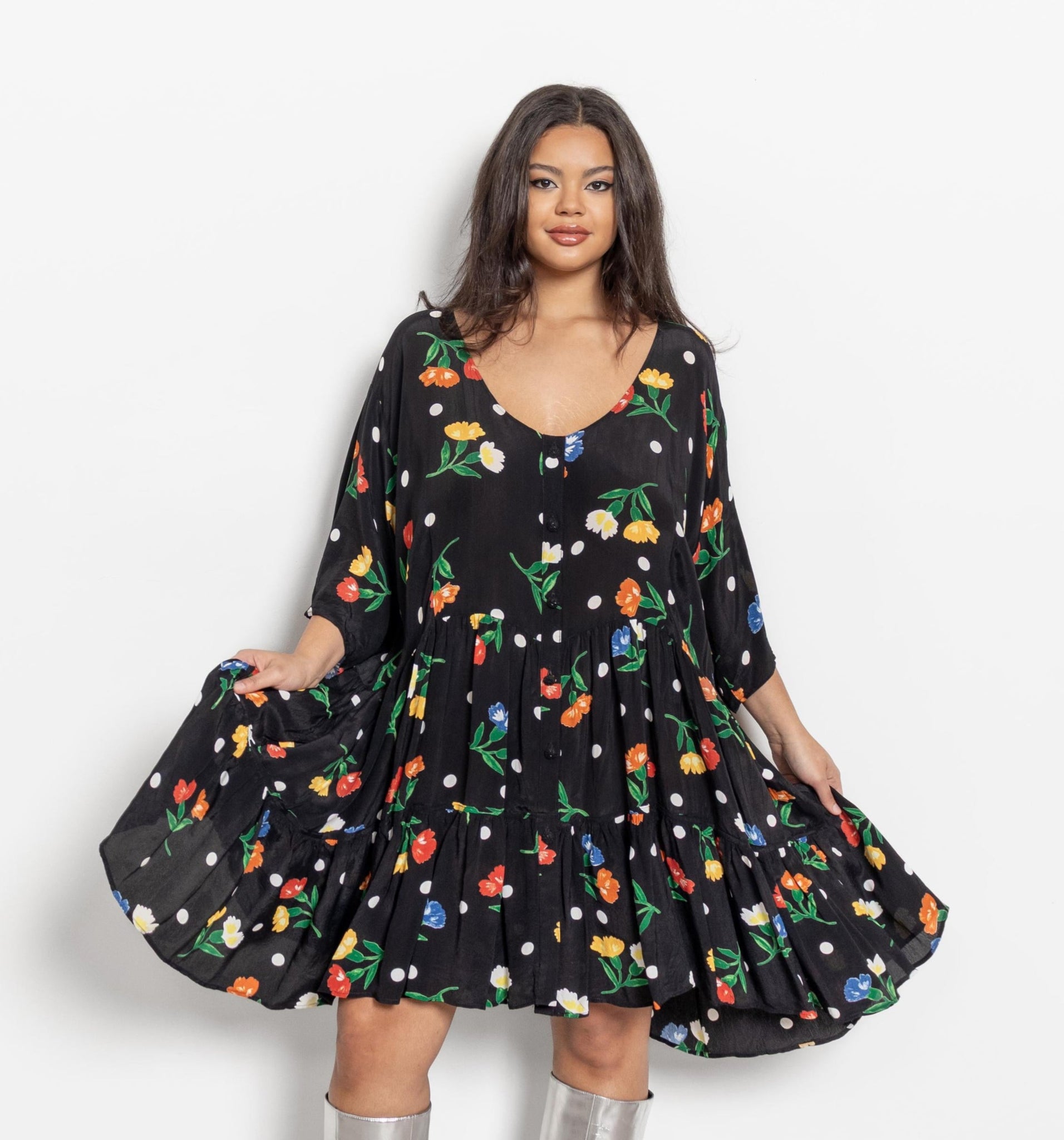 A person wearing a vintage black floral mini tent dress with short sleeves and buttons down the front. The dress is knee-length with a flared skirt.
