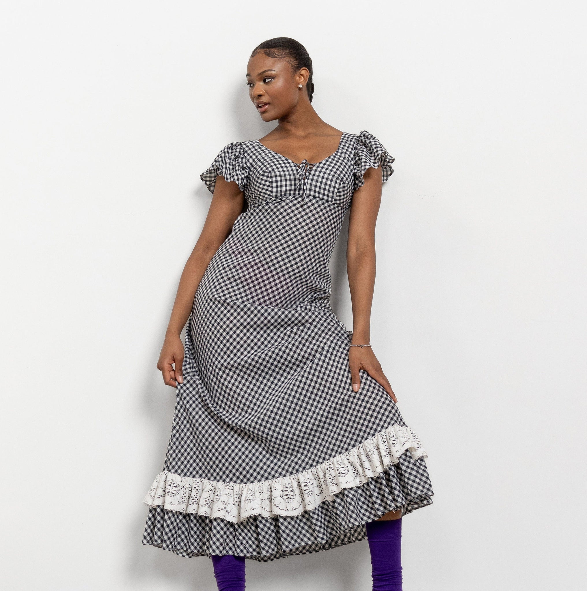 A vintage 90's black and white plaid maxi dress with ruffled cap sleeves and a ruffled bottom, featuring a checkered pattern. The dress is zippered at the back and displayed on a model mannequin.