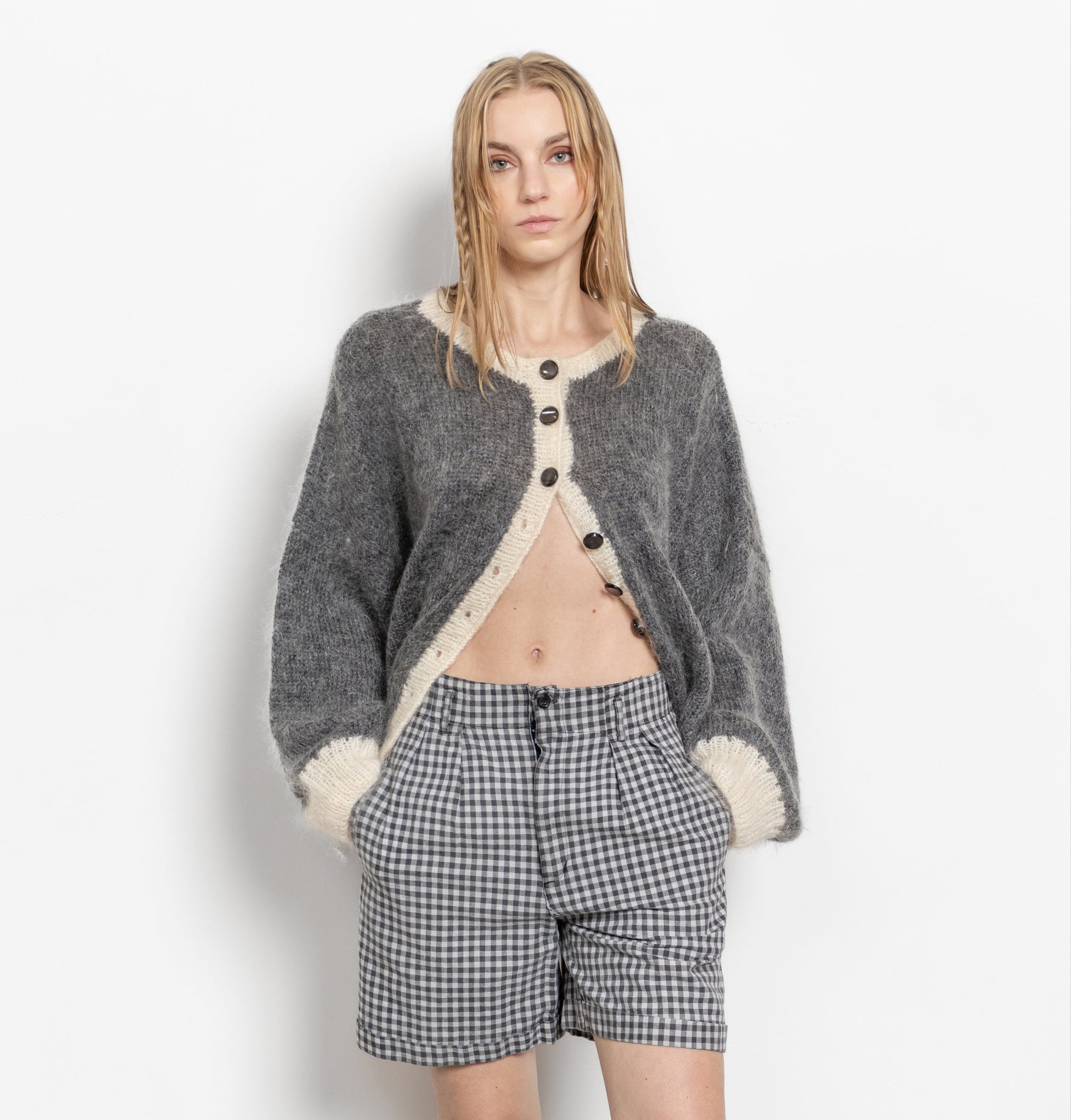 Person wearing a gray cardigan with white lining, plaid shorts, and silver boots on a white background