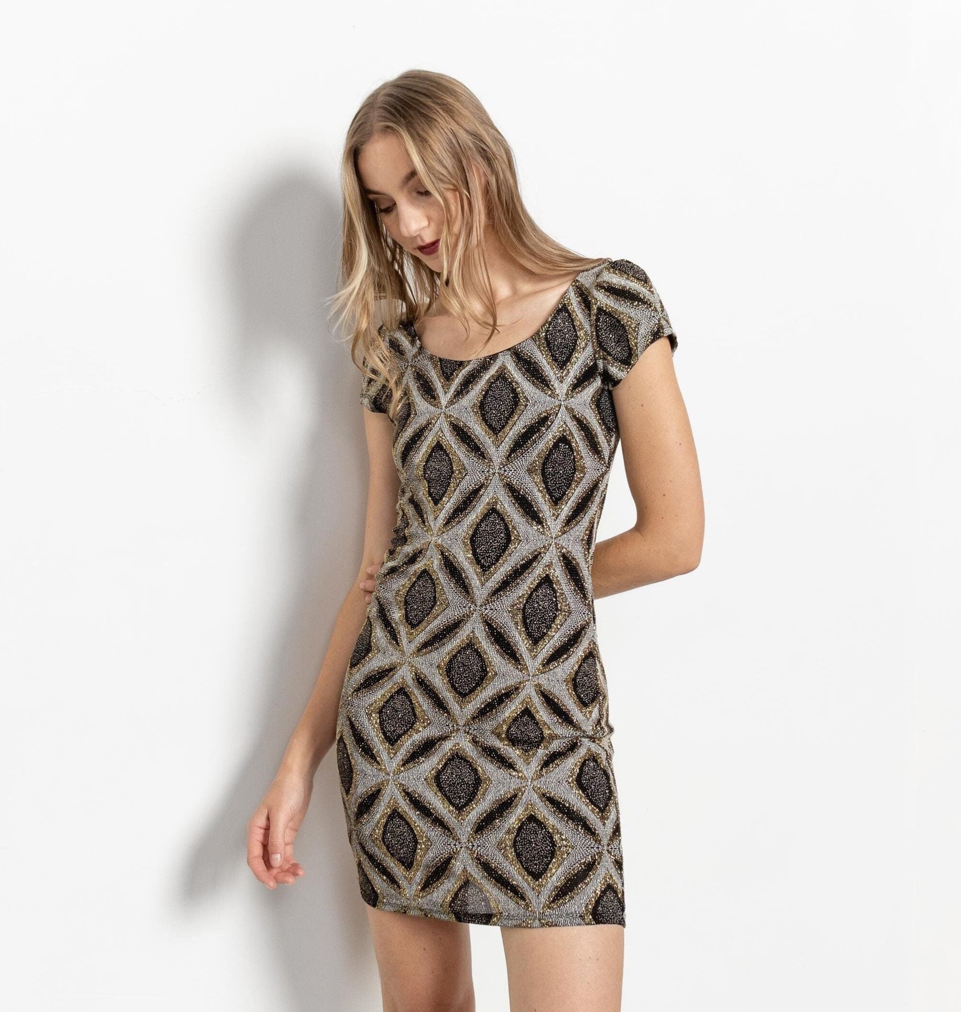 A model wearing a vintage 90's sparkly mini stretchy glitter dress with a black and grey diamond pattern, paired with white boots.