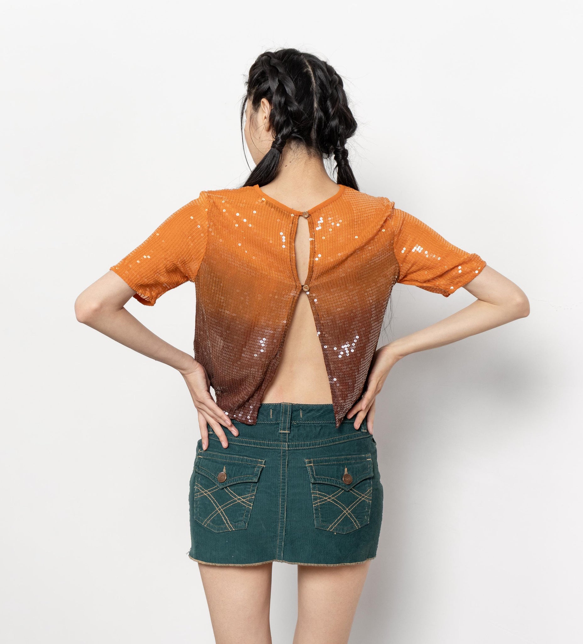 Woman wearing an orange sequin top and green denim skirt on a white background