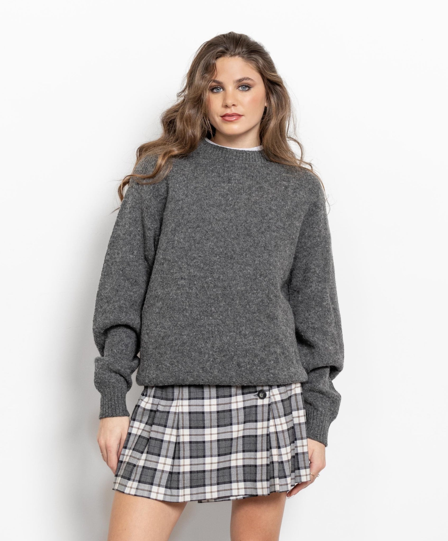 A female model wearing a heather grey vintage pullover sweater with a crew neckline and long sleeves, paired with a plaid mini skirt and white boots.