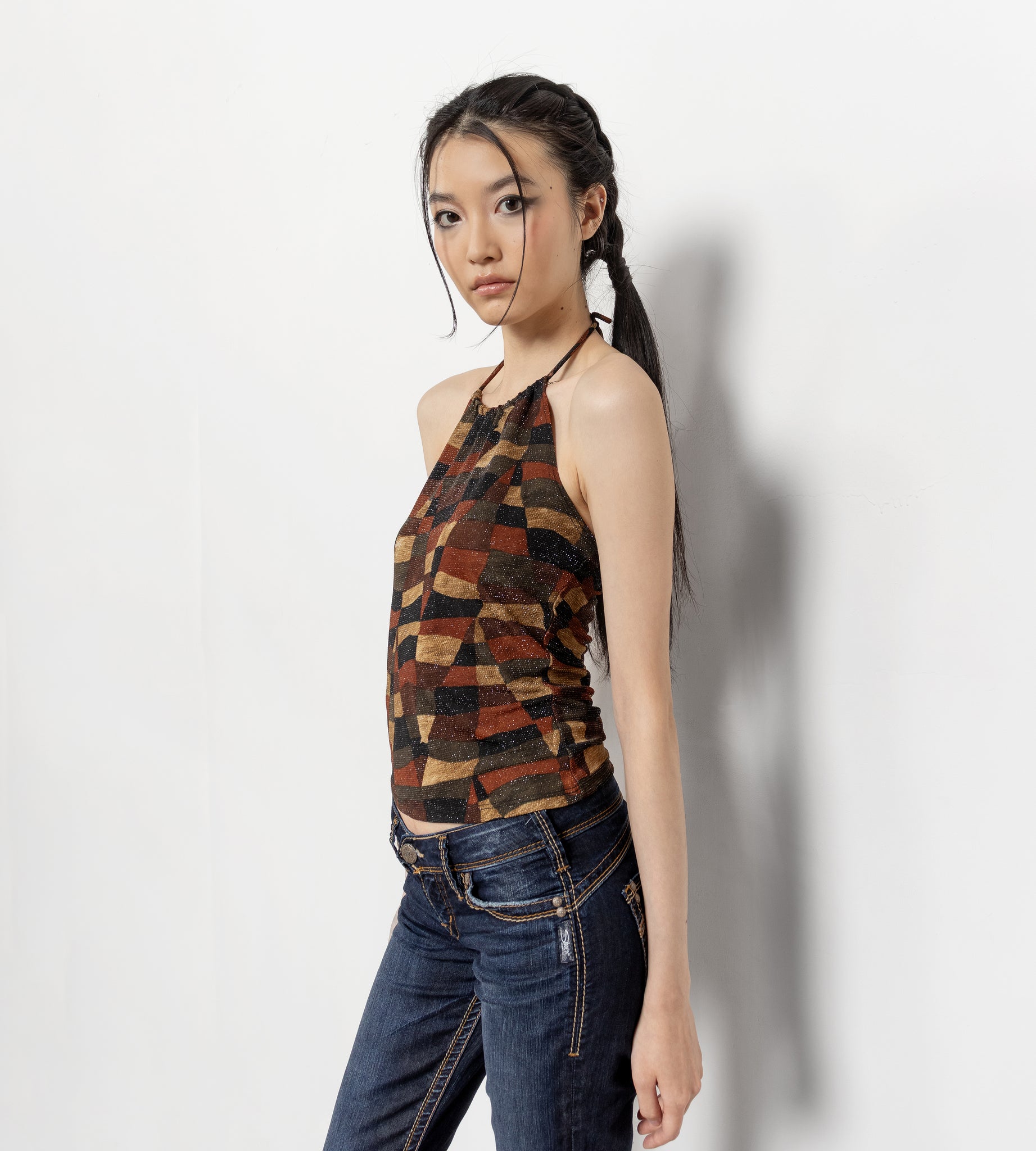 Woman wearing a patterned top and jeans against a white background