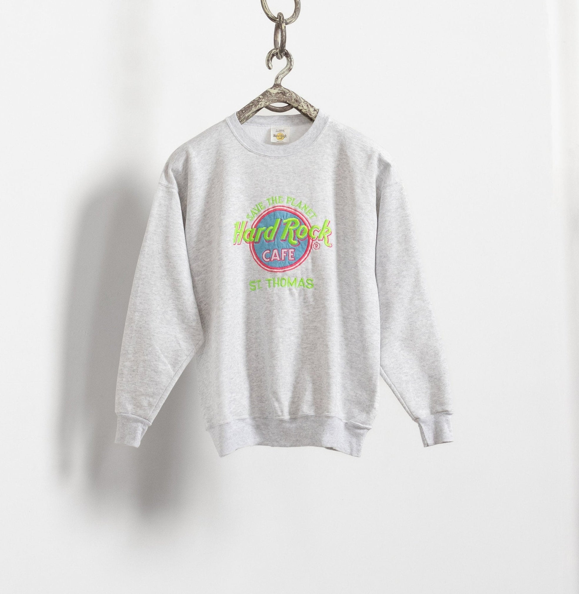 A heather grey pullover sweatshirt with the 'Hard Rock Cafe' logo in blue, green, and pink embroidery, hanging on a hanger against a white wall.