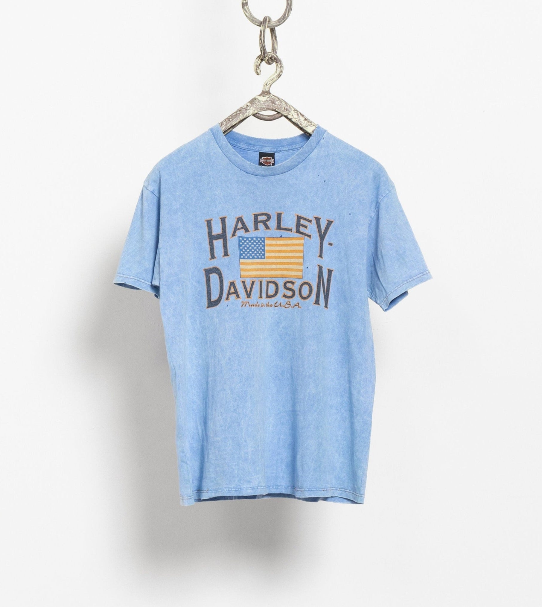 A blue Harley Davidson t-shirt hanging from a chain, displaying the brand's logo and the text 'Harley Davidson' on the front.