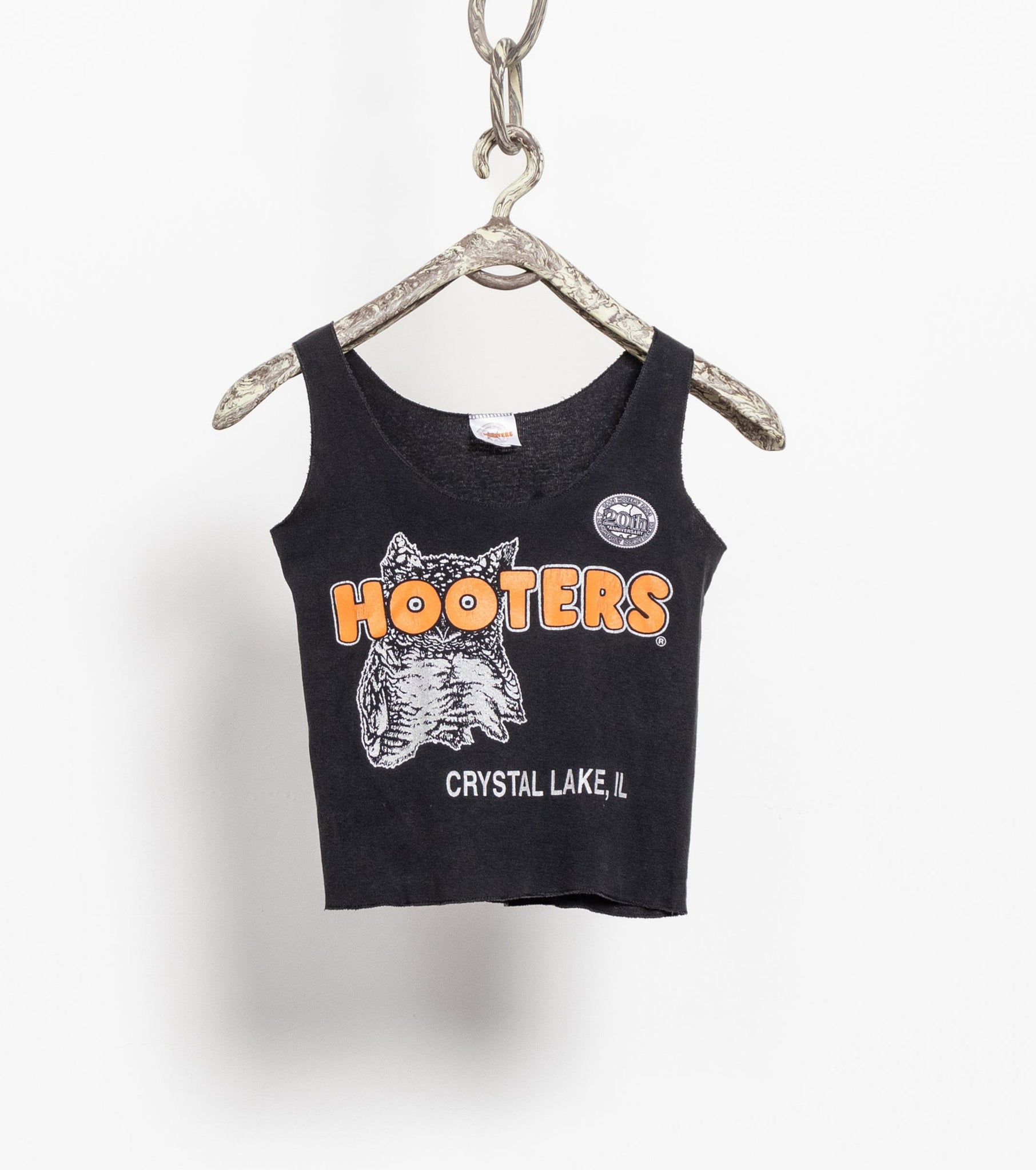 Vintage Hooters baby tank top in black with a large silver owl on the front, displayed on a chain hangar.