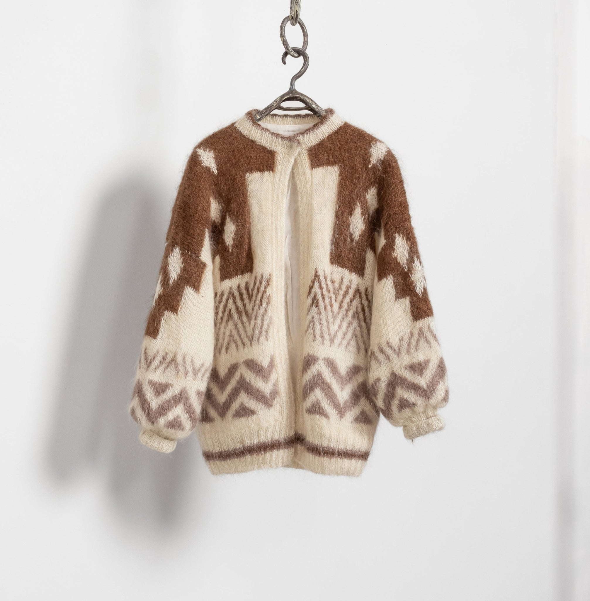 A vintage Icelandic wool cardigan in beige and brown colors with a geometric pattern, displayed on a hanger against a white background.