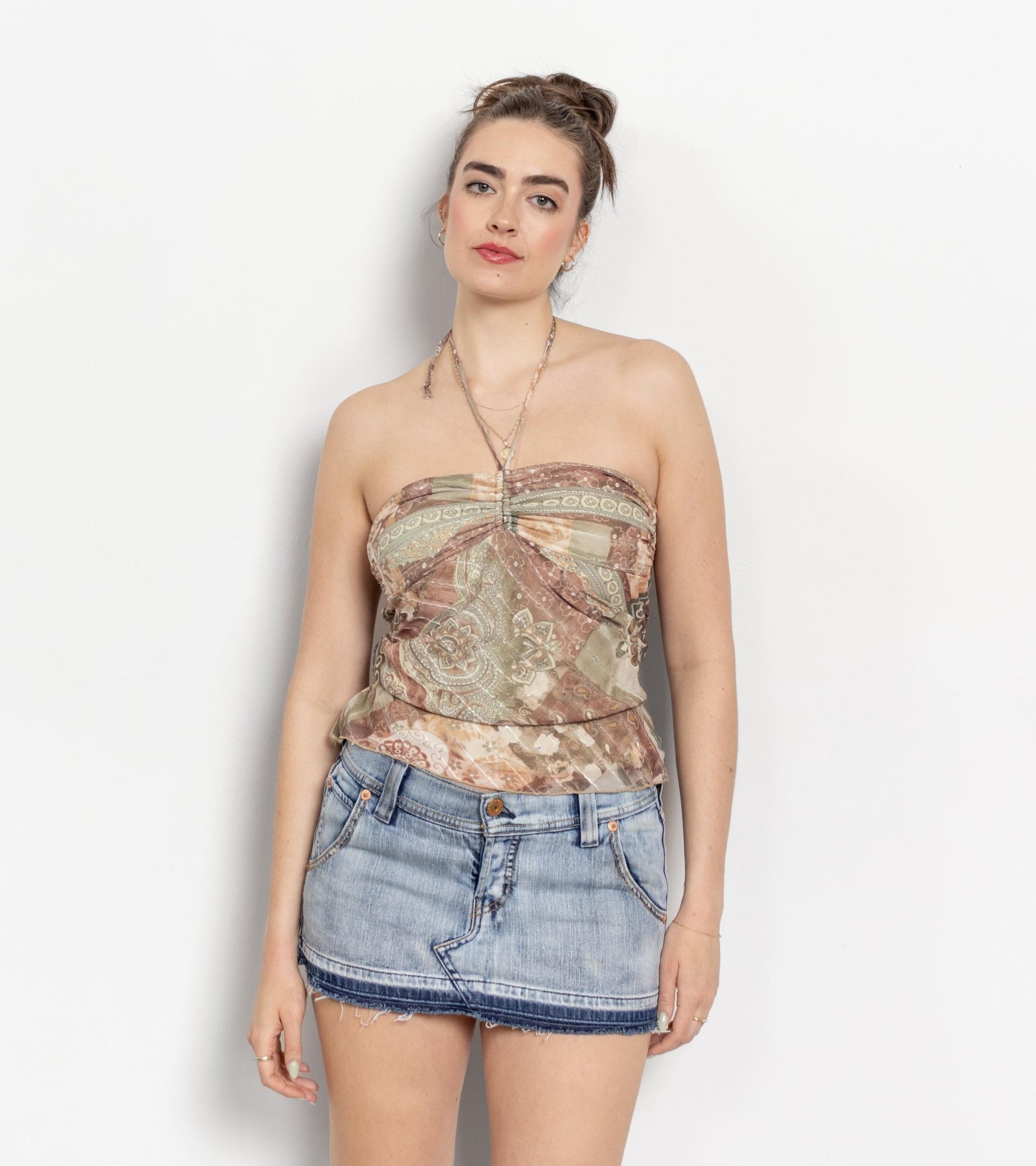 Woman wearing a patterned strapless top and denim shorts on a white background