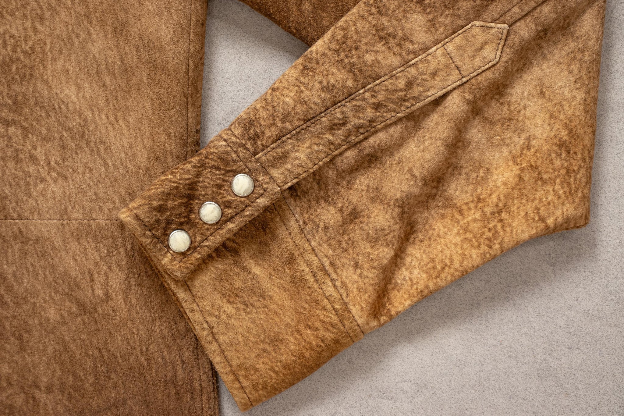Close-up of a brown leather jacket with buttons on a neutral background