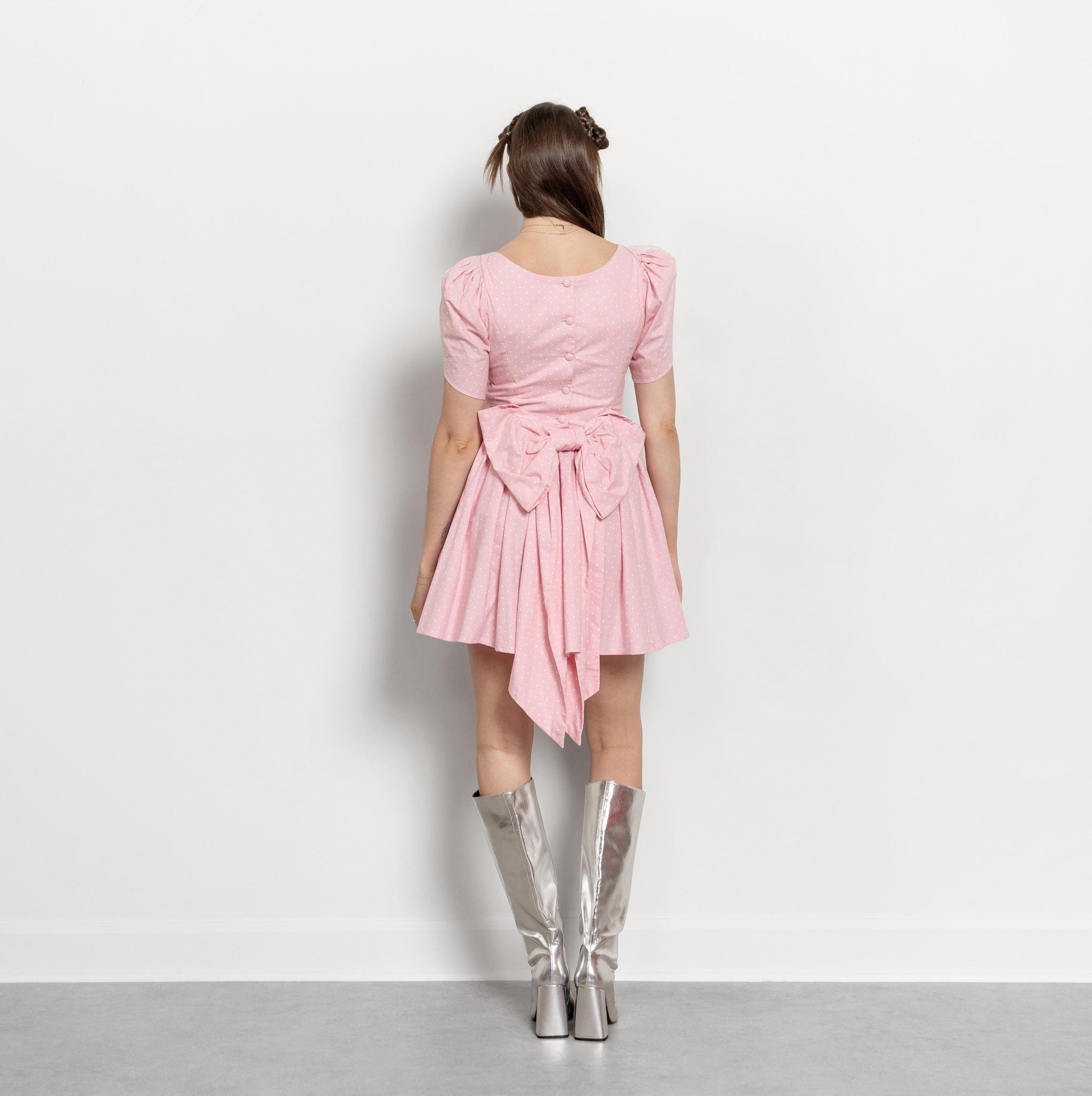 Woman wearing a pink dress with a bow and silver knee-high boots on a light gray background