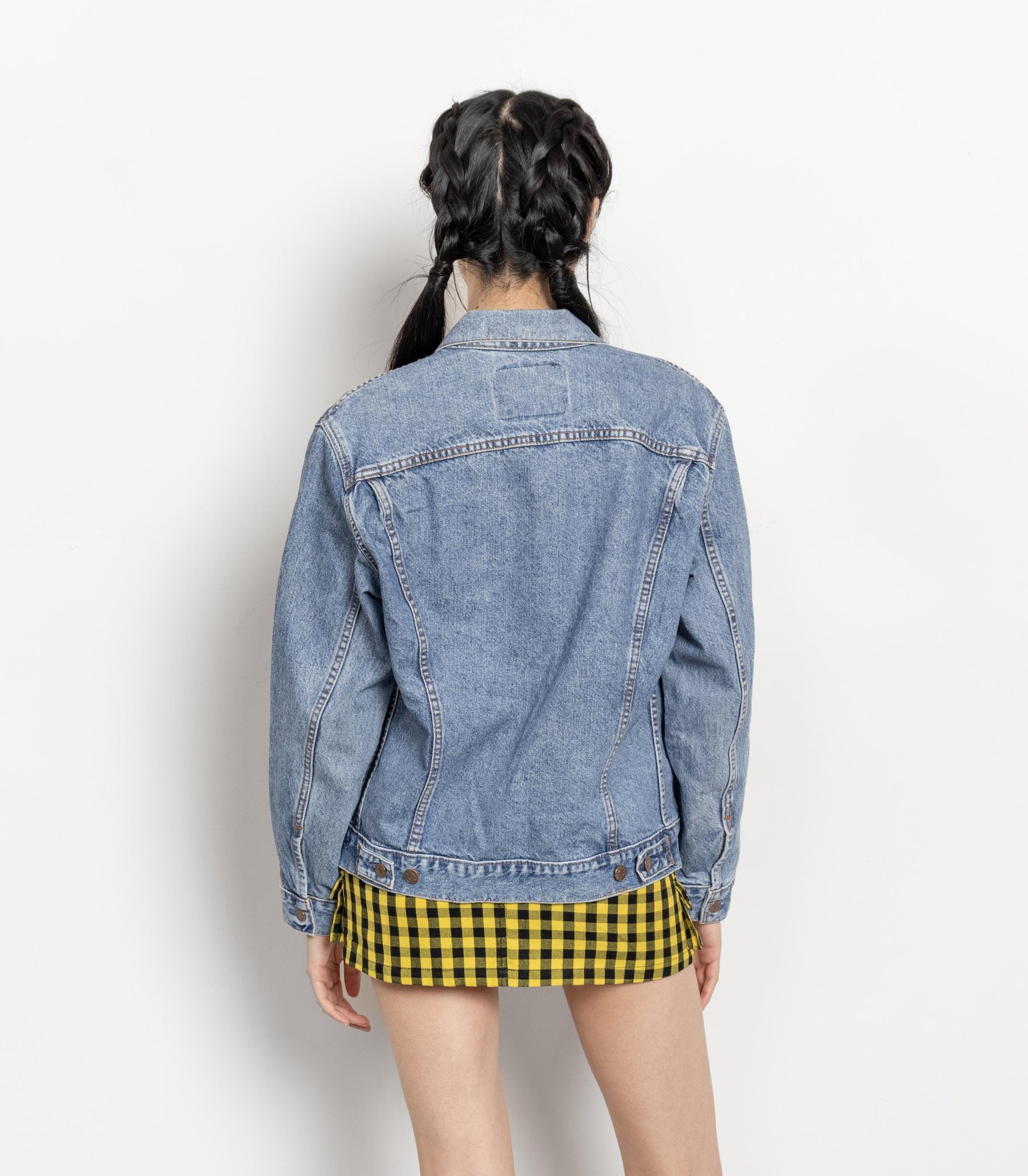 Person wearing a denim jacket and yellow checkered skirt on a white background