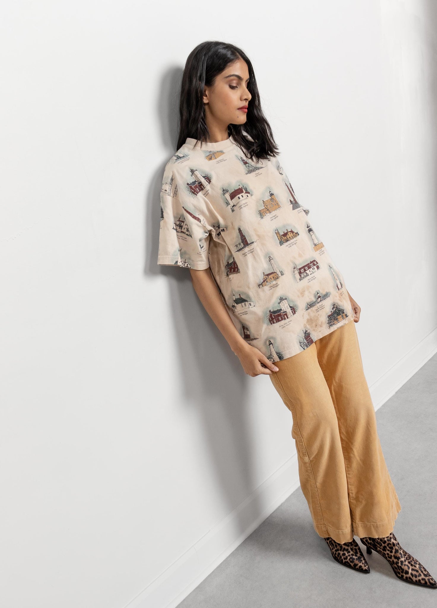 Woman wearing a patterned shirt and beige pants against a white background