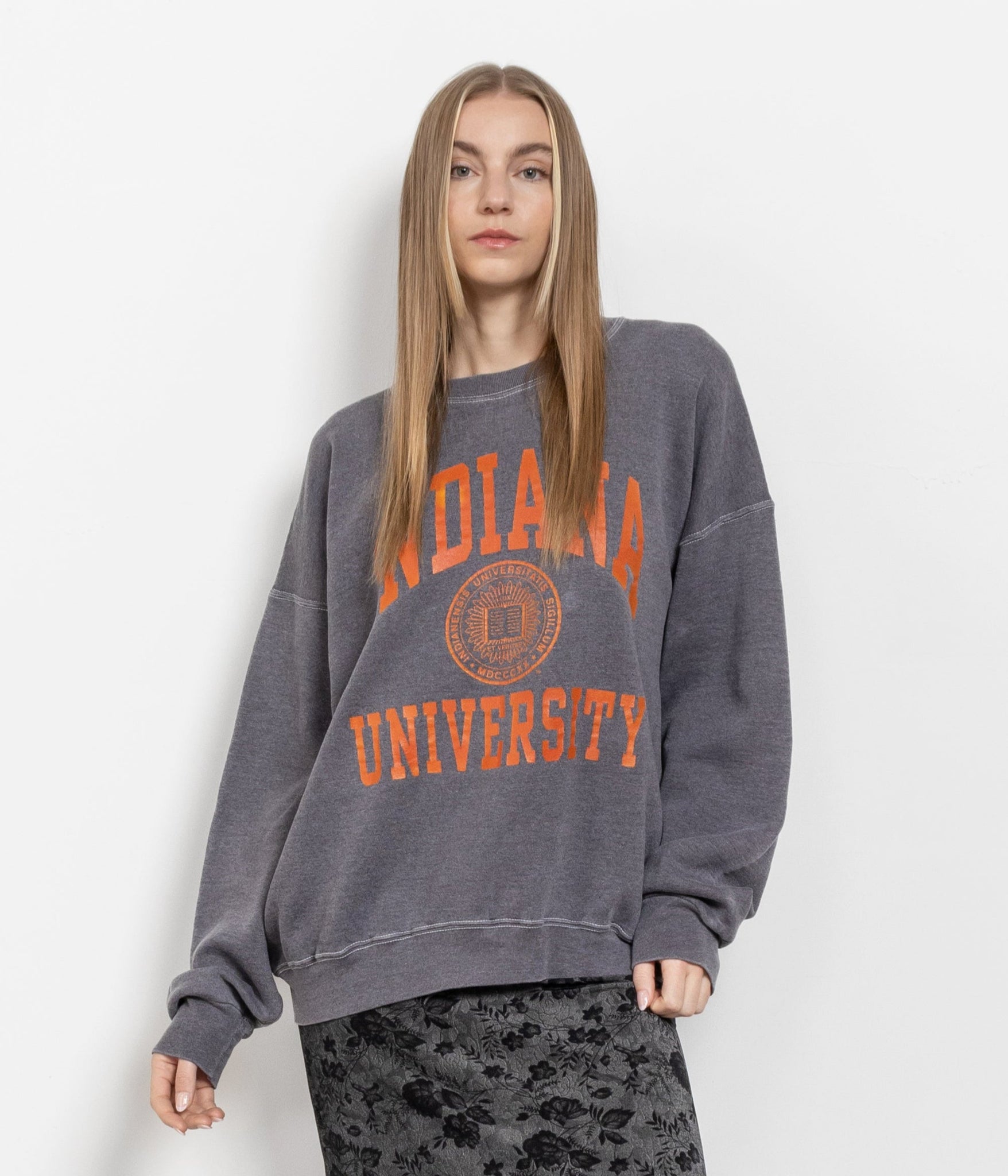 A person wearing a vintage gray Indiana University pullover sweatshirt with orange lettering, paired with a patterned skirt.