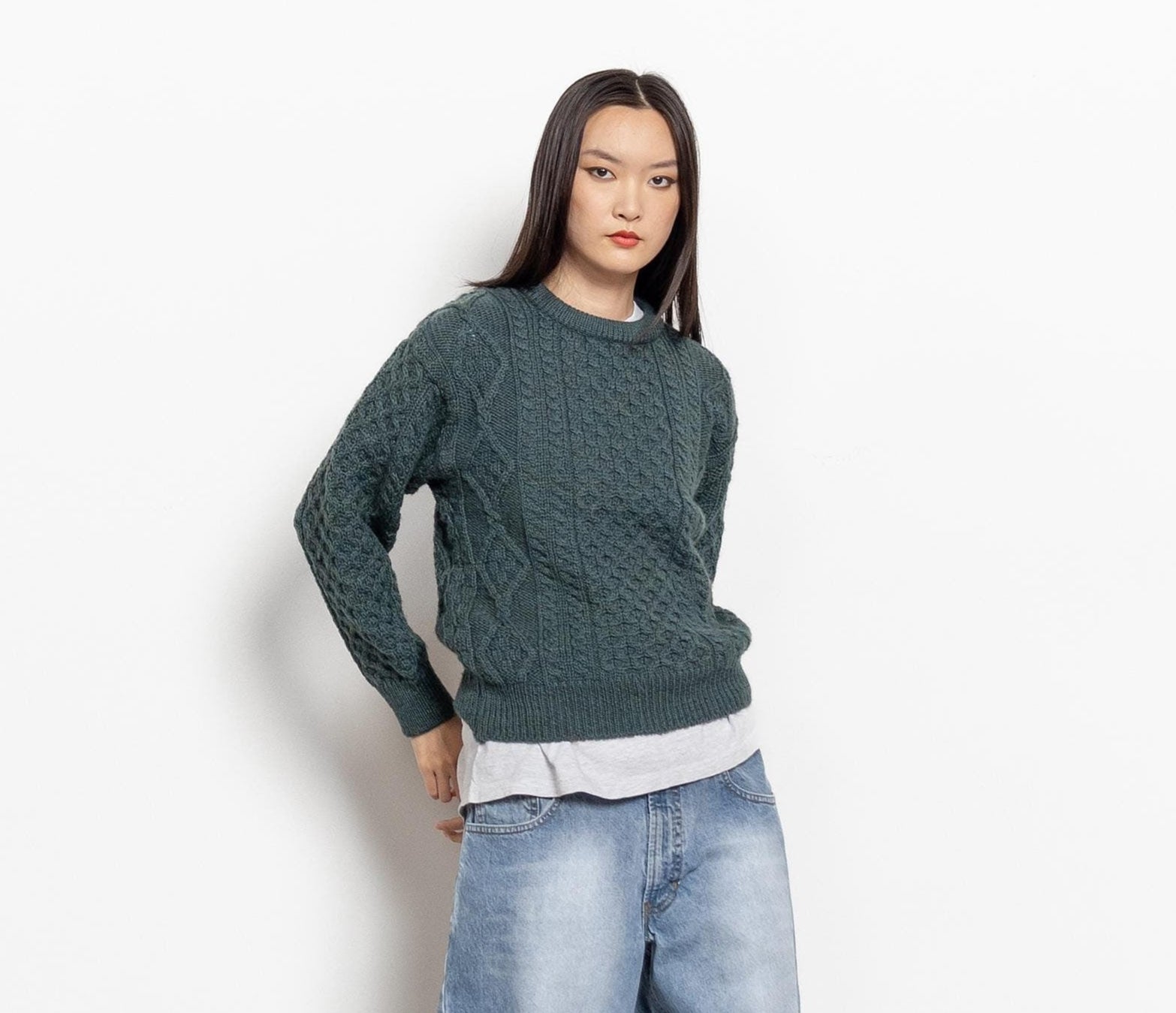 Person wearing a green sweater and blue jeans standing against a white background