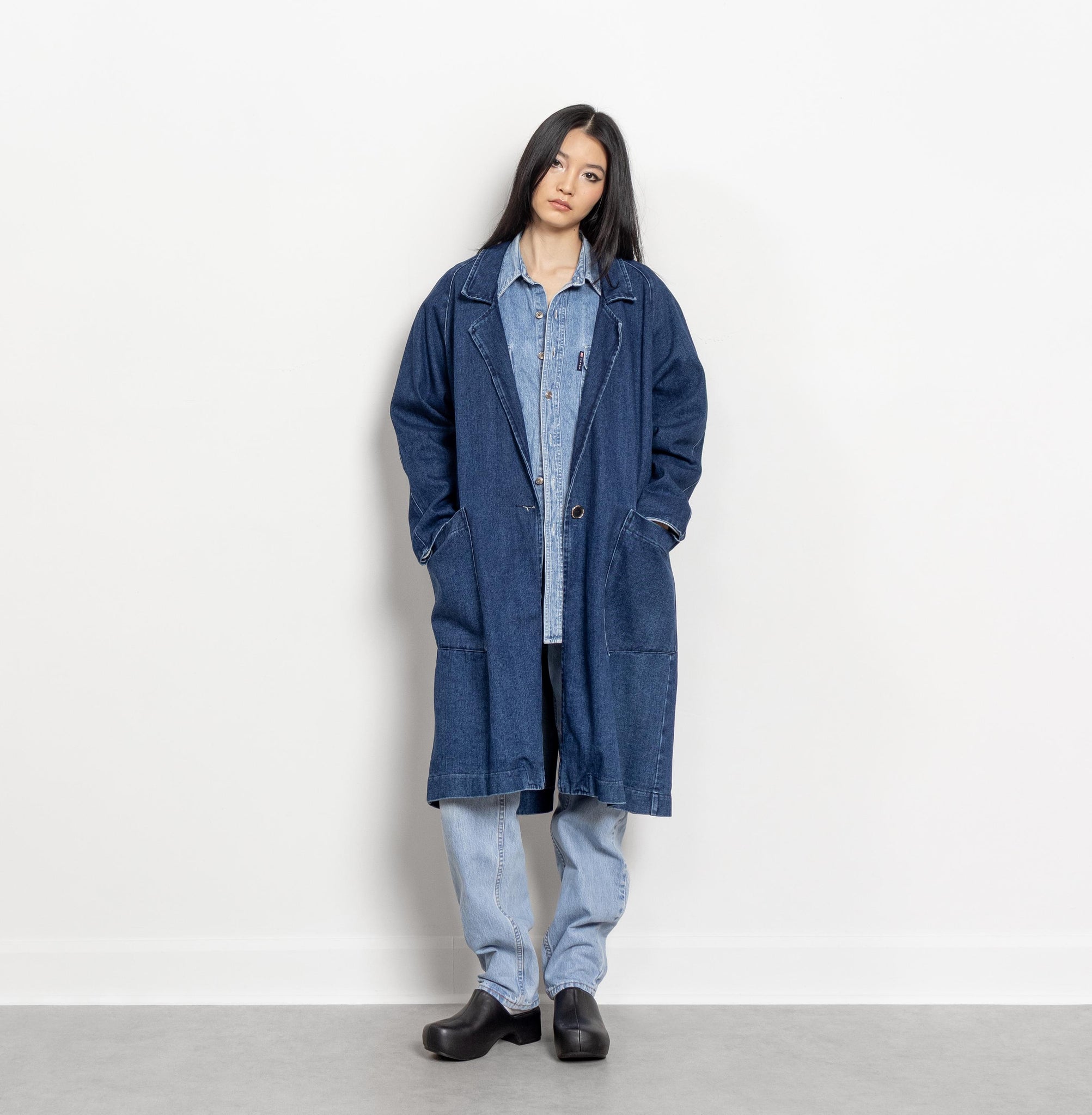 Person wearing a long blue coat over a denim outfit on a white background
