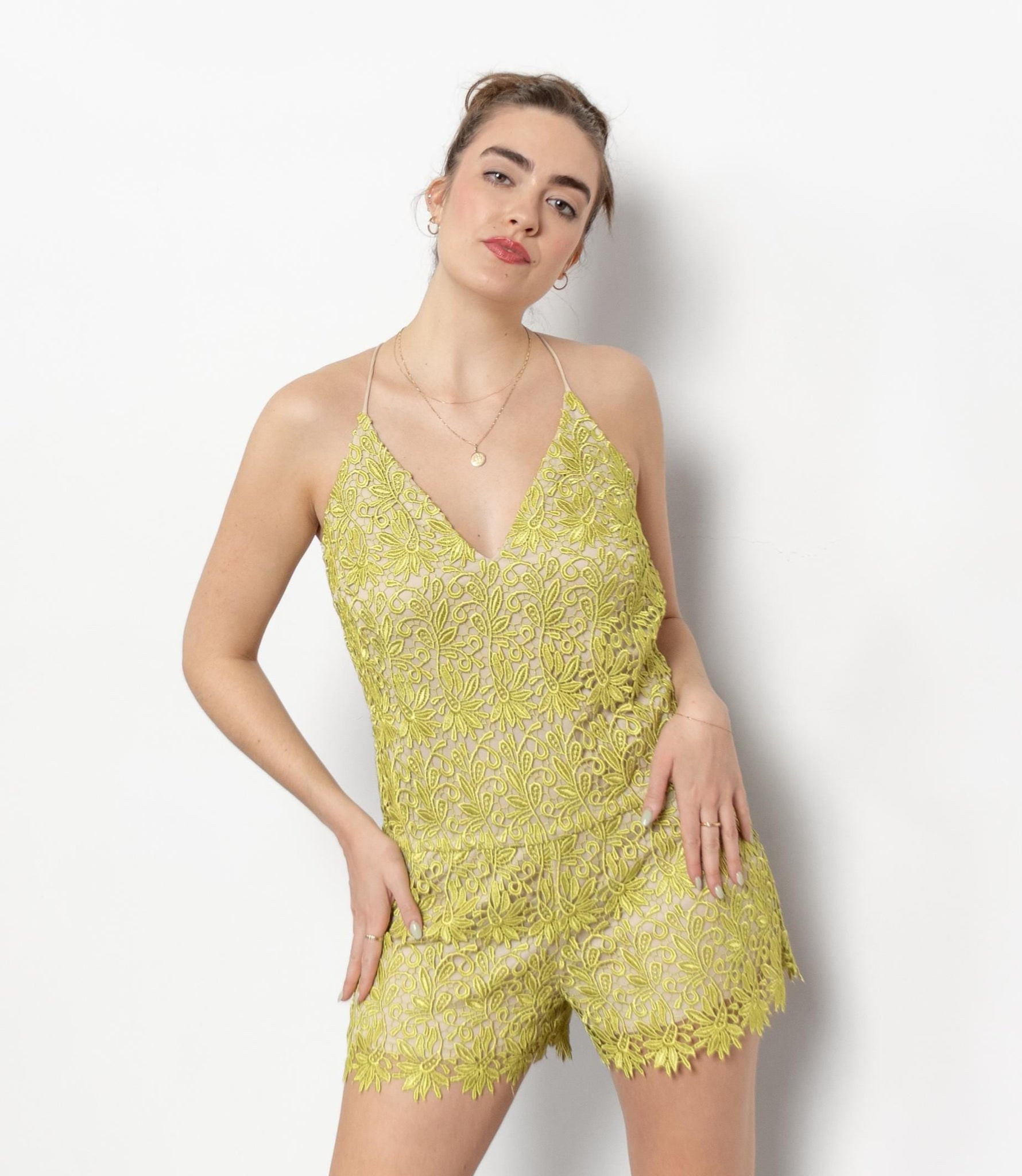 Woman wearing a yellow lace romper with silver high-heeled boots against a white background