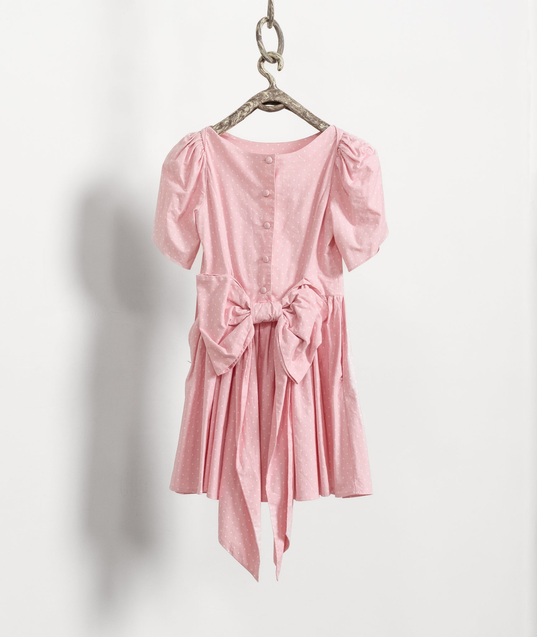 Pink dress with puff sleeves and a bow tie hanging on a white background