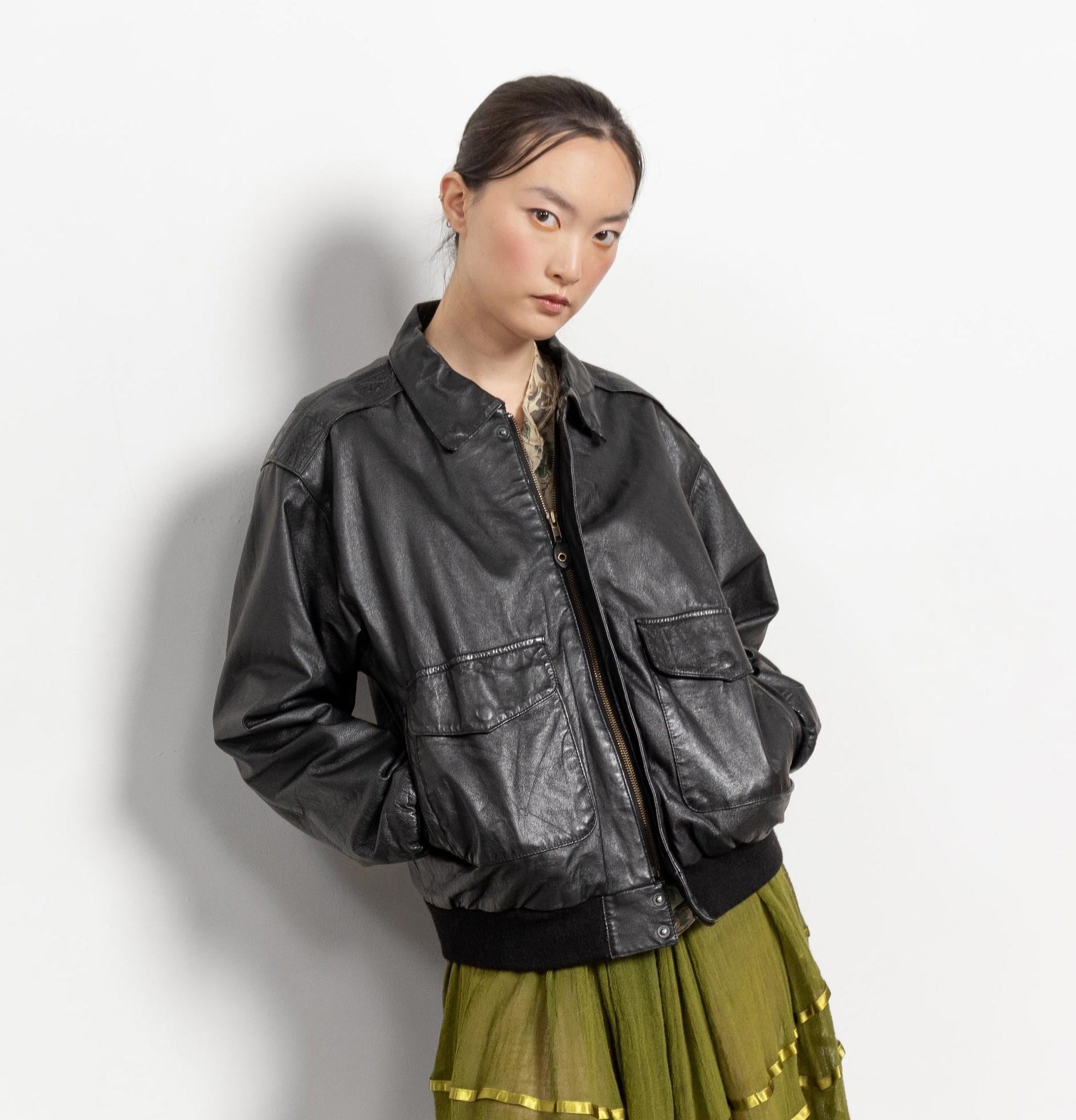 Person wearing a black leather jacket and green skirt against a white background