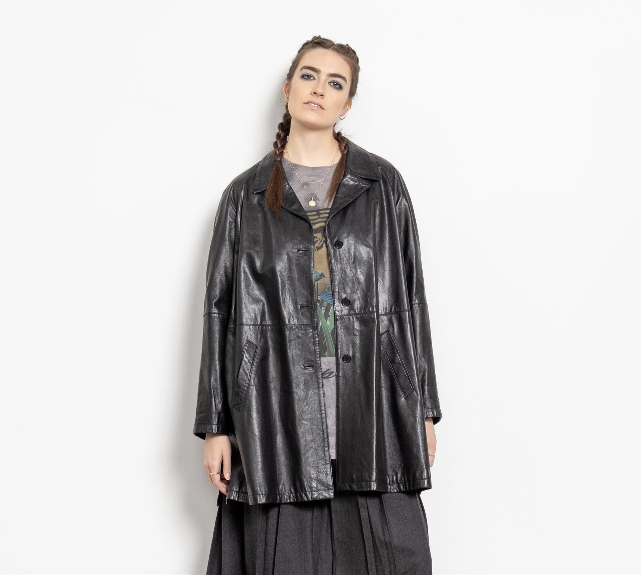 A person wearing a vintage 90's black leather jacket with oversized fit, side pockets, and buttons down the front. The jacket is on a person standing against a plain background.