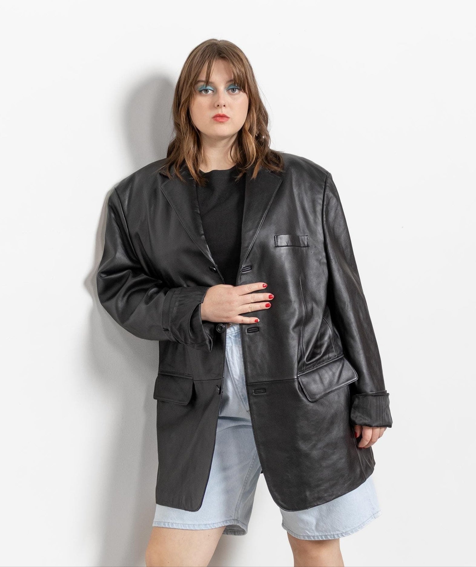 Woman wearing a black leather jacket, black top, denim shorts, and gray boots against a white background