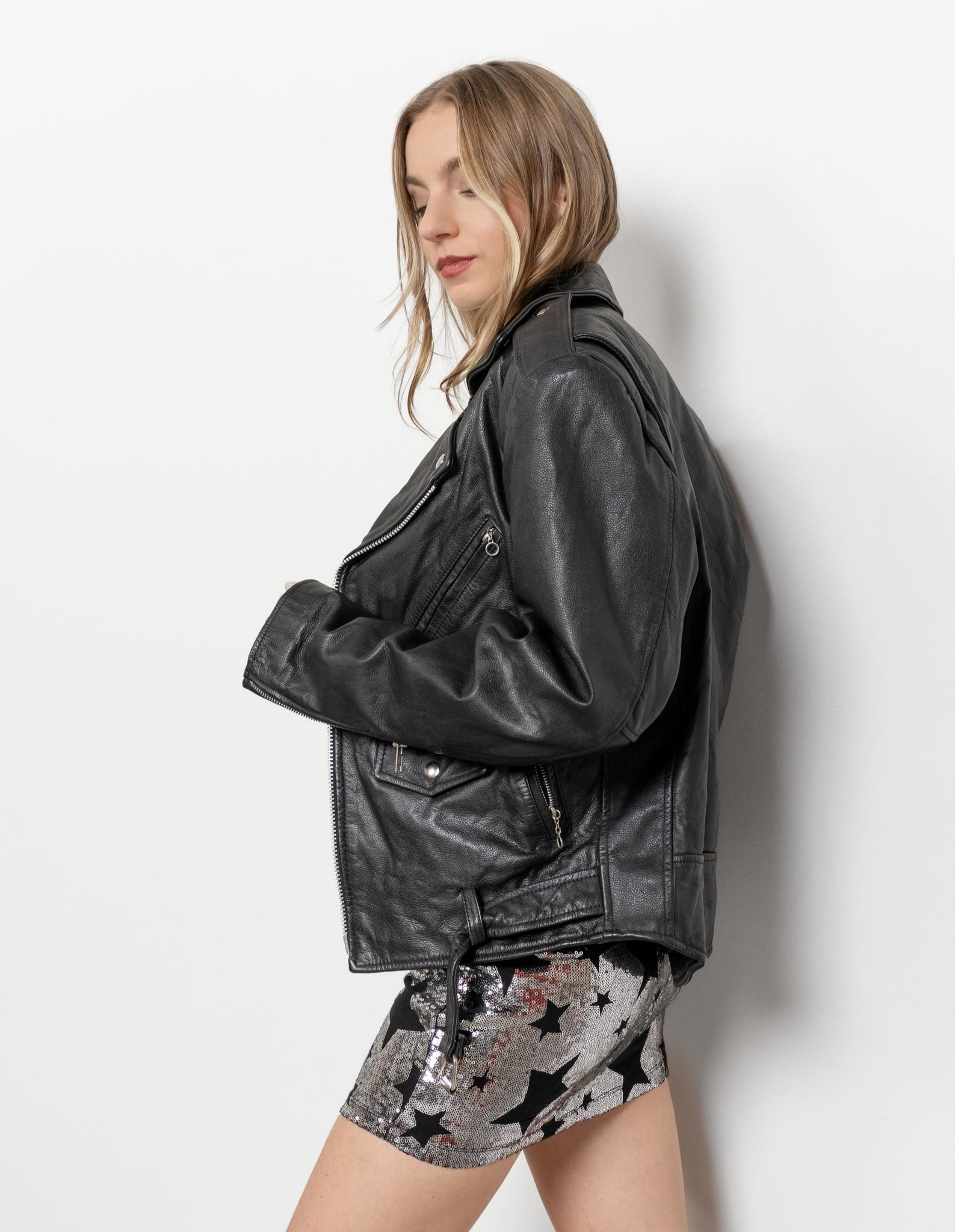 Woman wearing a black leather jacket and star-patterned shorts against a white background