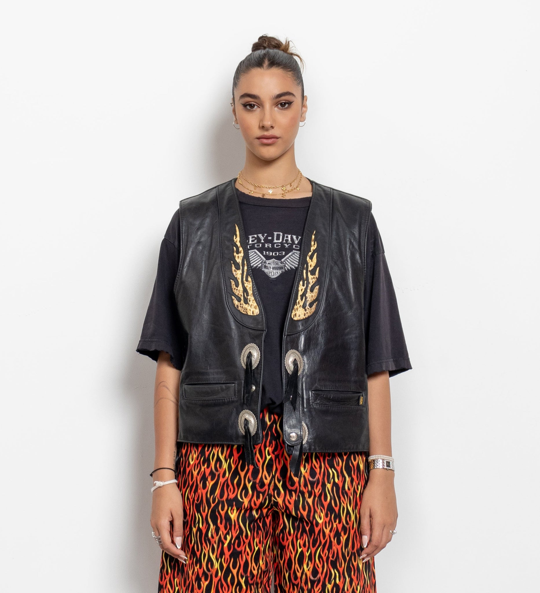 Person wearing a black leather jacket, black shirt with graphic design, and colorful patterned pants on a white background